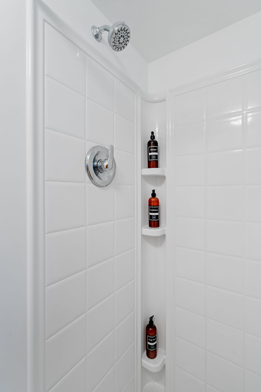 A sleek, modern shower area featuring white tiles and neatly arranged bath products.