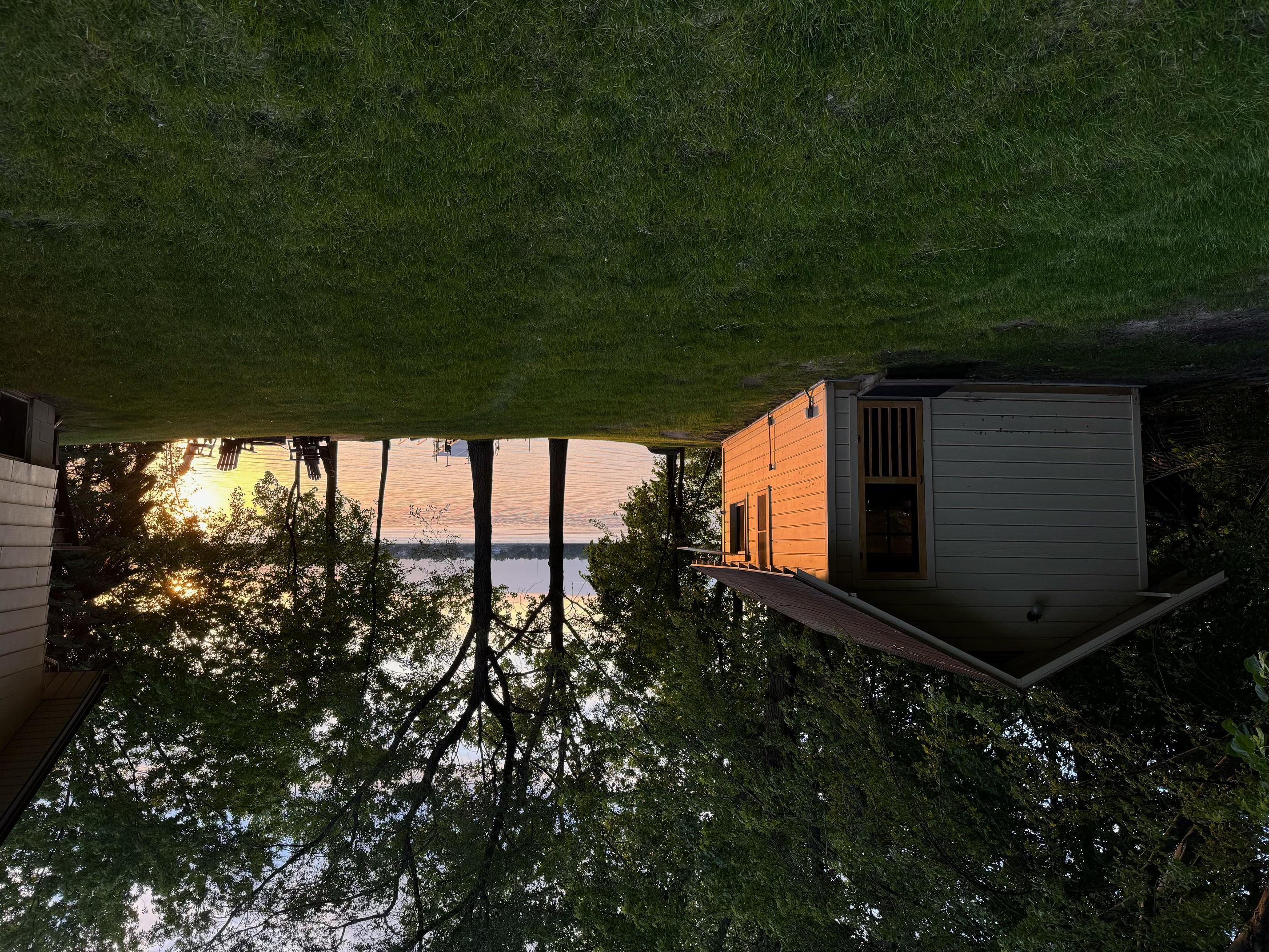 A cozy cabin by the lake at sunset, surrounded by greenery.