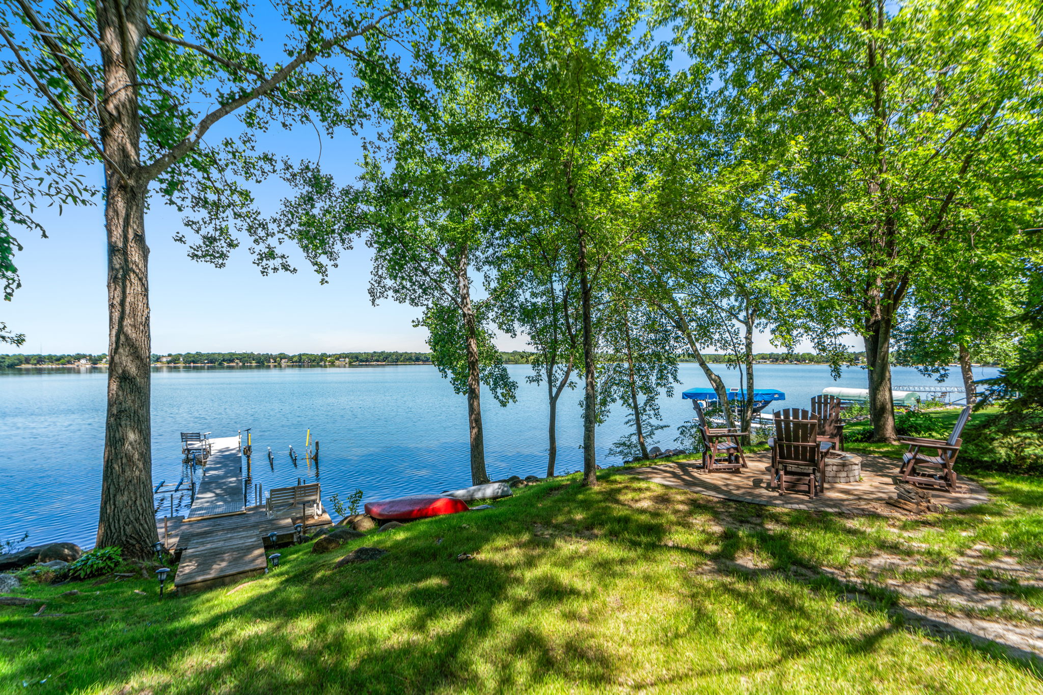 A tranquil lakeside scene with green trees, a wooden dock, and a cozy seating area.