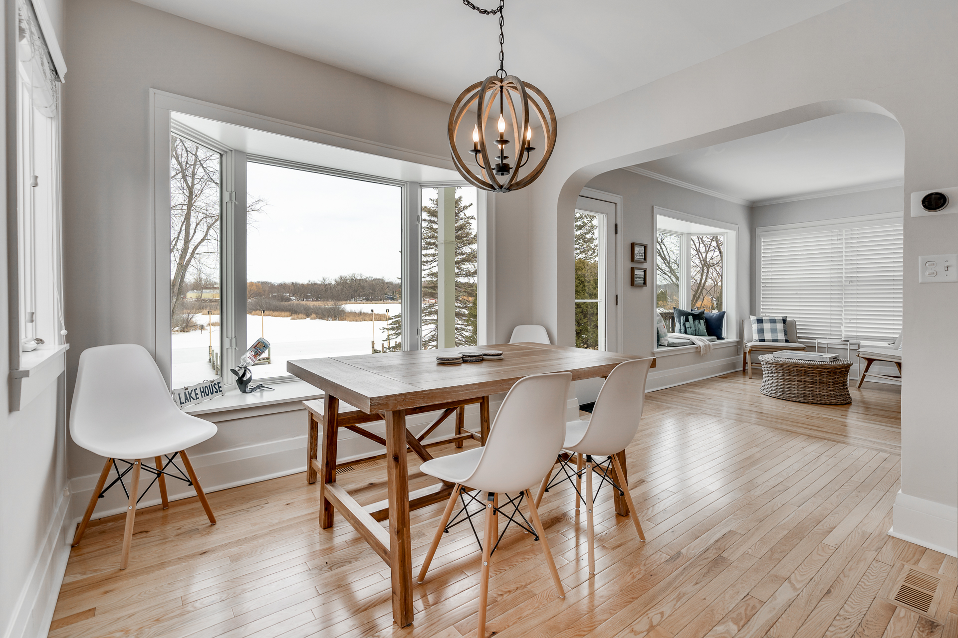 A bright dining area with a wooden table and modern white chairs, overlooking a scenic view.