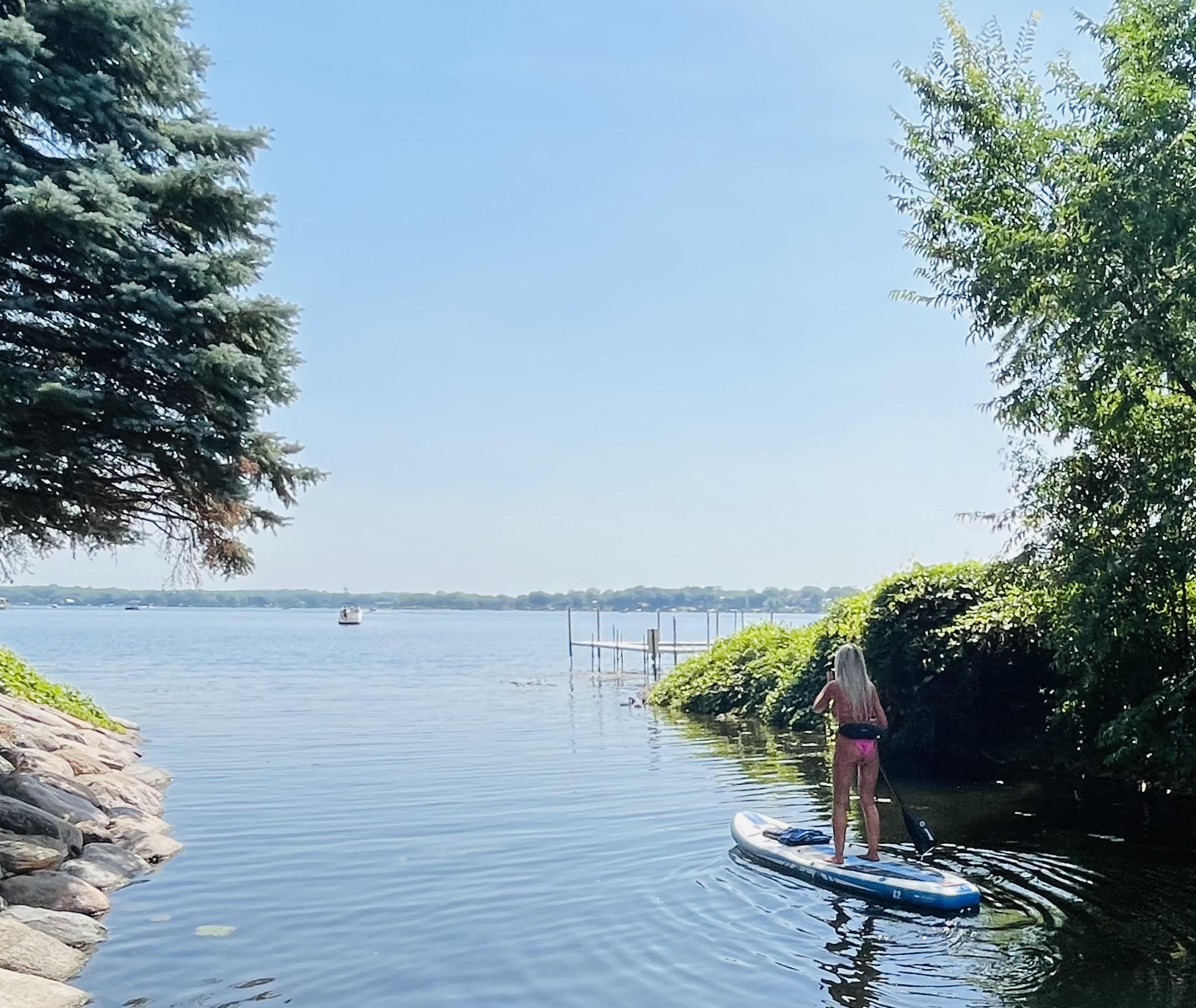 A young woman enjoying paddleboarding on a peaceful lake under a clear blue sky.