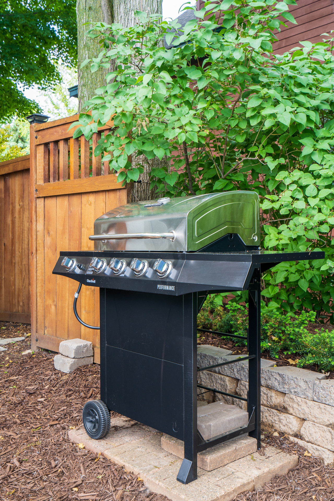 A black gas grill with a sleek silver lid set against a lush green backdrop in a backyard.