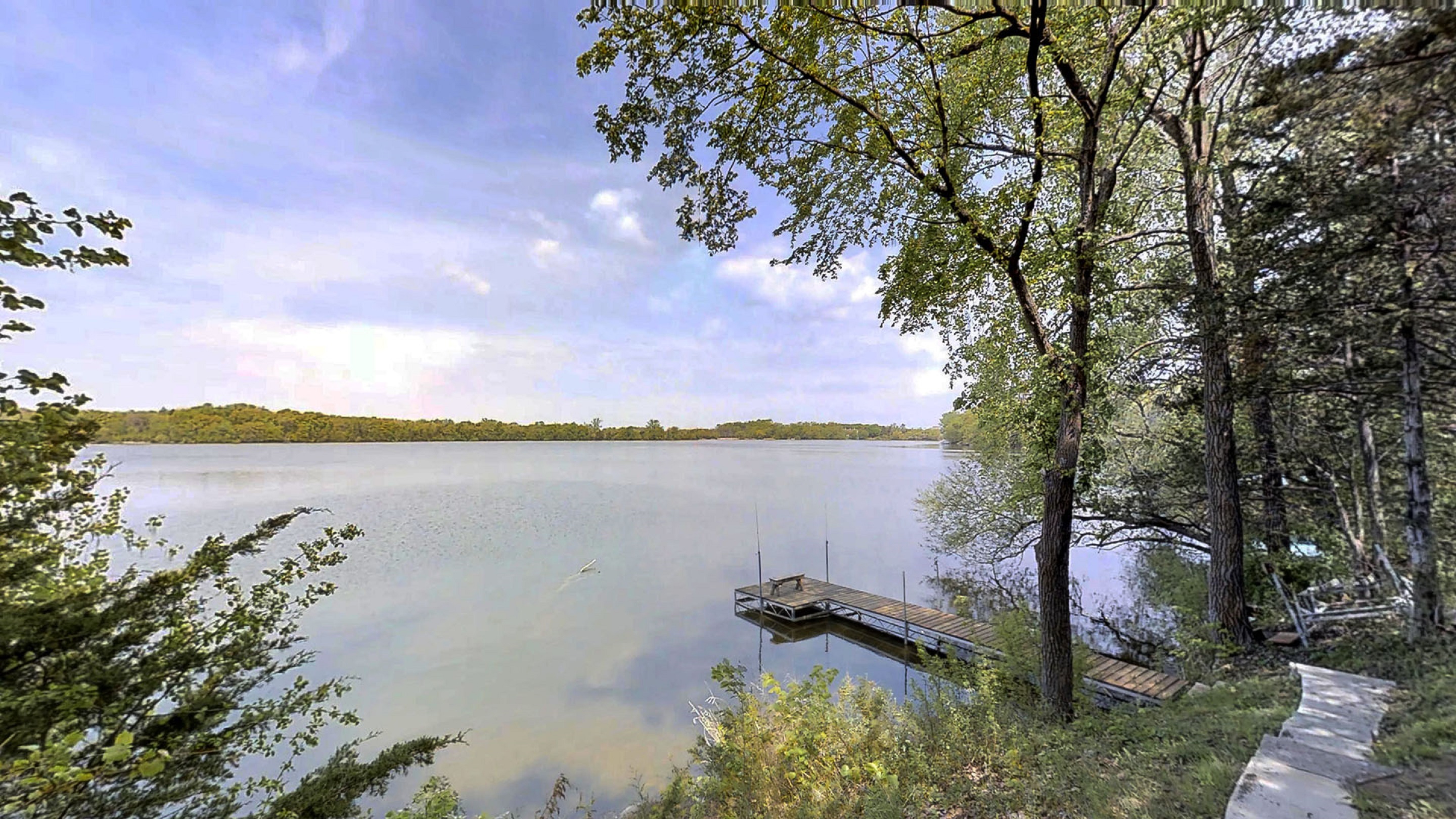 A tranquil lakeside view featuring a wooden dock and lush greenery.
