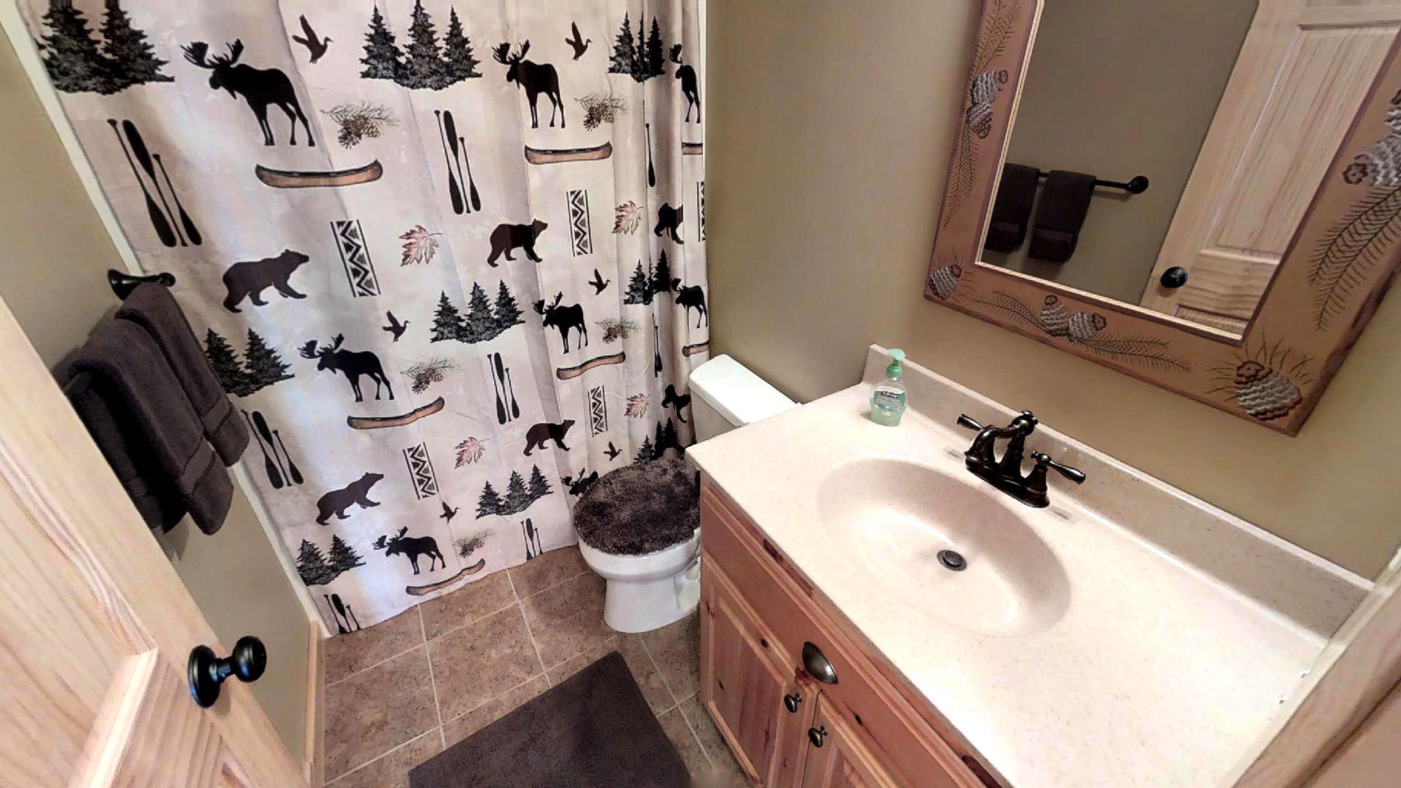 A rustic-themed bathroom featuring a nature-inspired shower curtain and wooden accents.