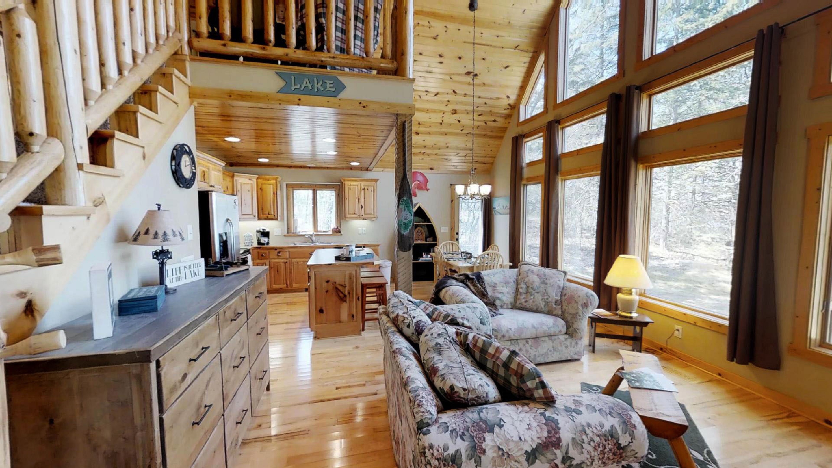 A cozy wooden cabin living room with floral sofas and a view of nature.