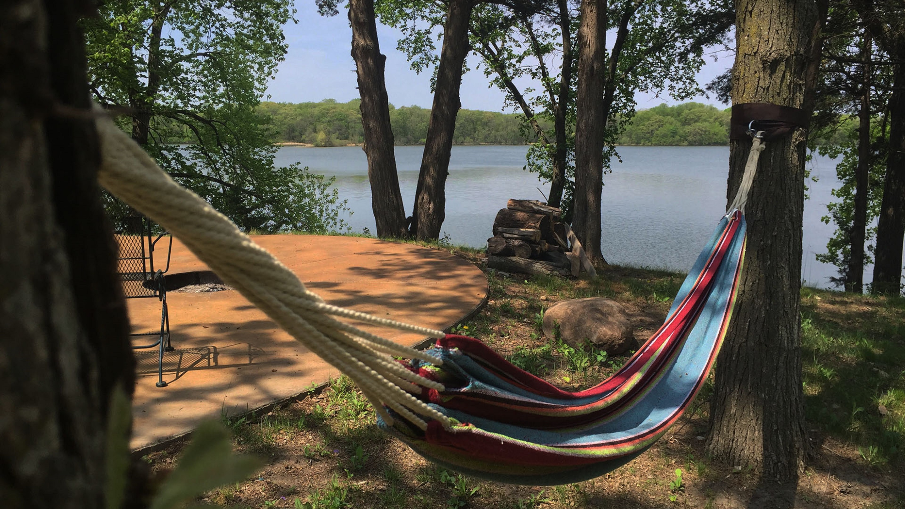 A colorful hammock nestled between trees by a tranquil lake.