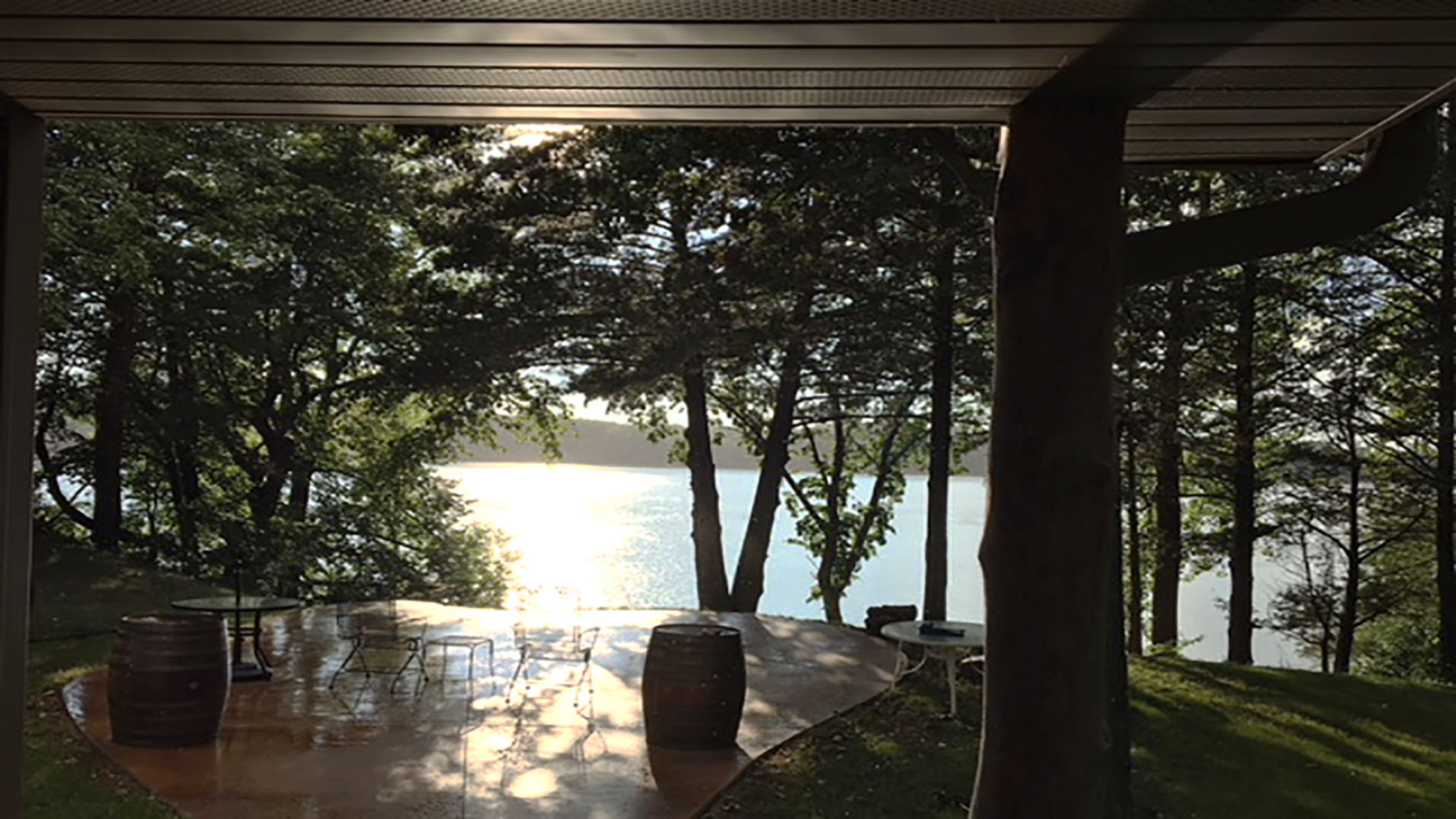 A tranquil lakeside view from a covered patio with rustic seating.