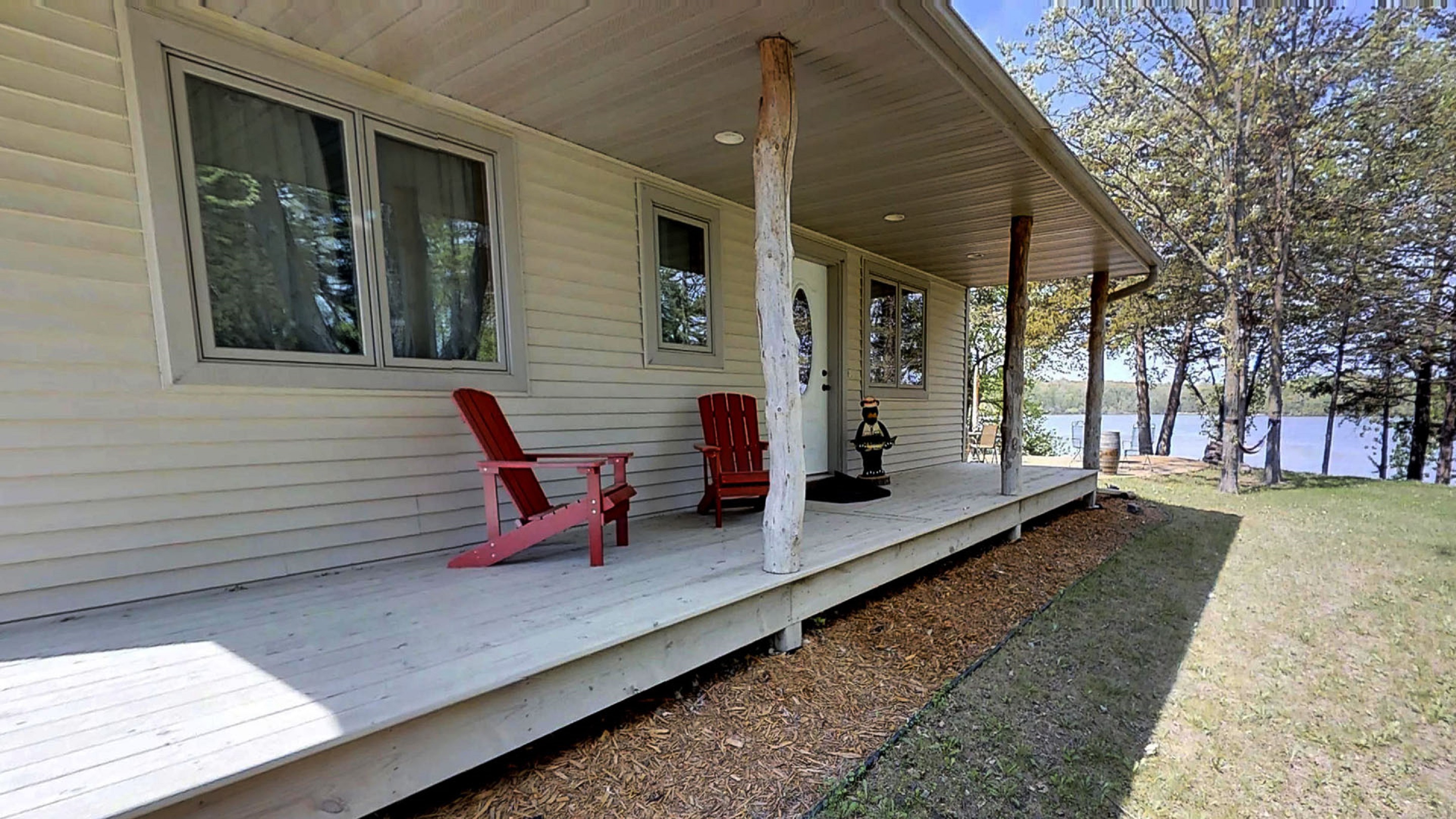 A cozy lakeside home featuring red adirondack chairs on a wooden porch.