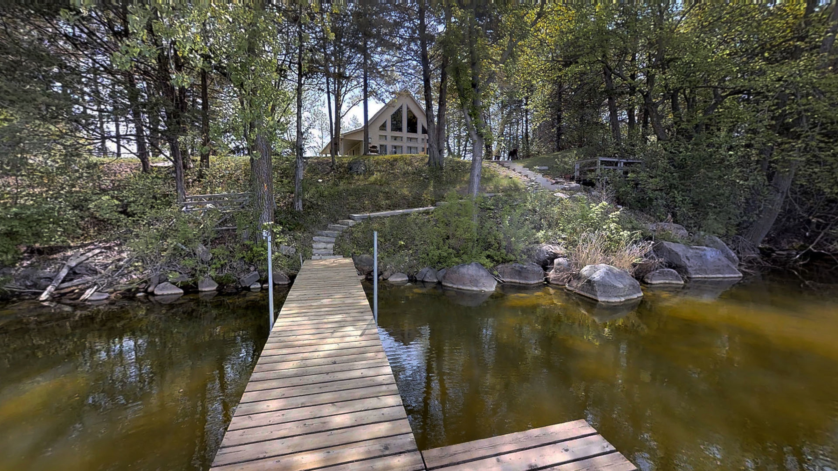 Lakeside view featuring a wooden dock and an A-frame house among trees.