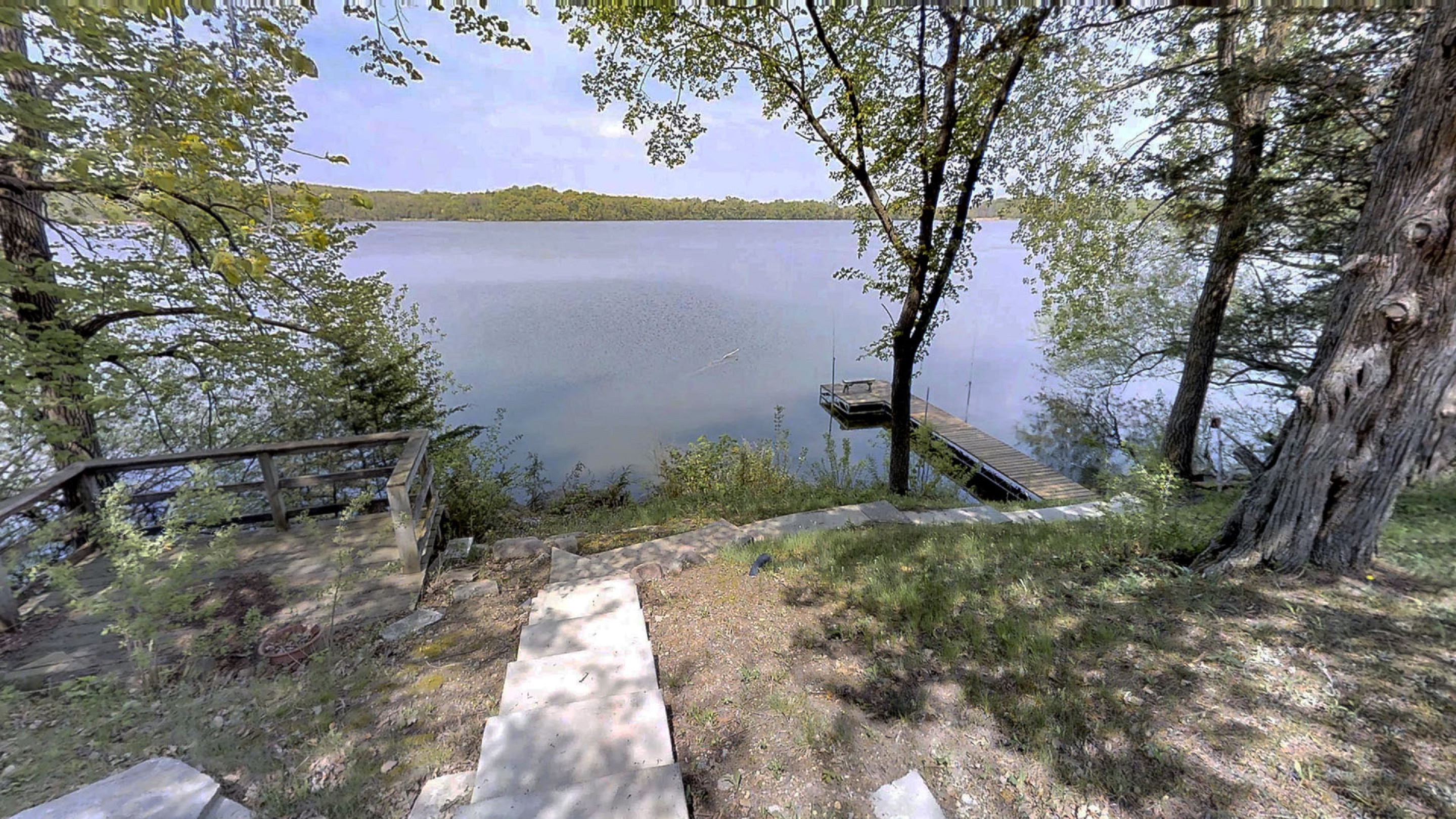 A tranquil lakeside view with a wooden dock and lush greenery.