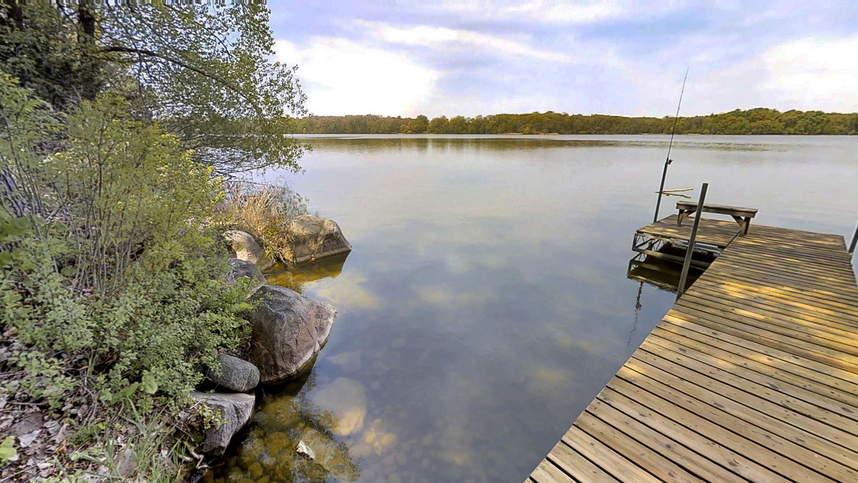 A tranquil lakeside view featuring a wooden dock and lush greenery.