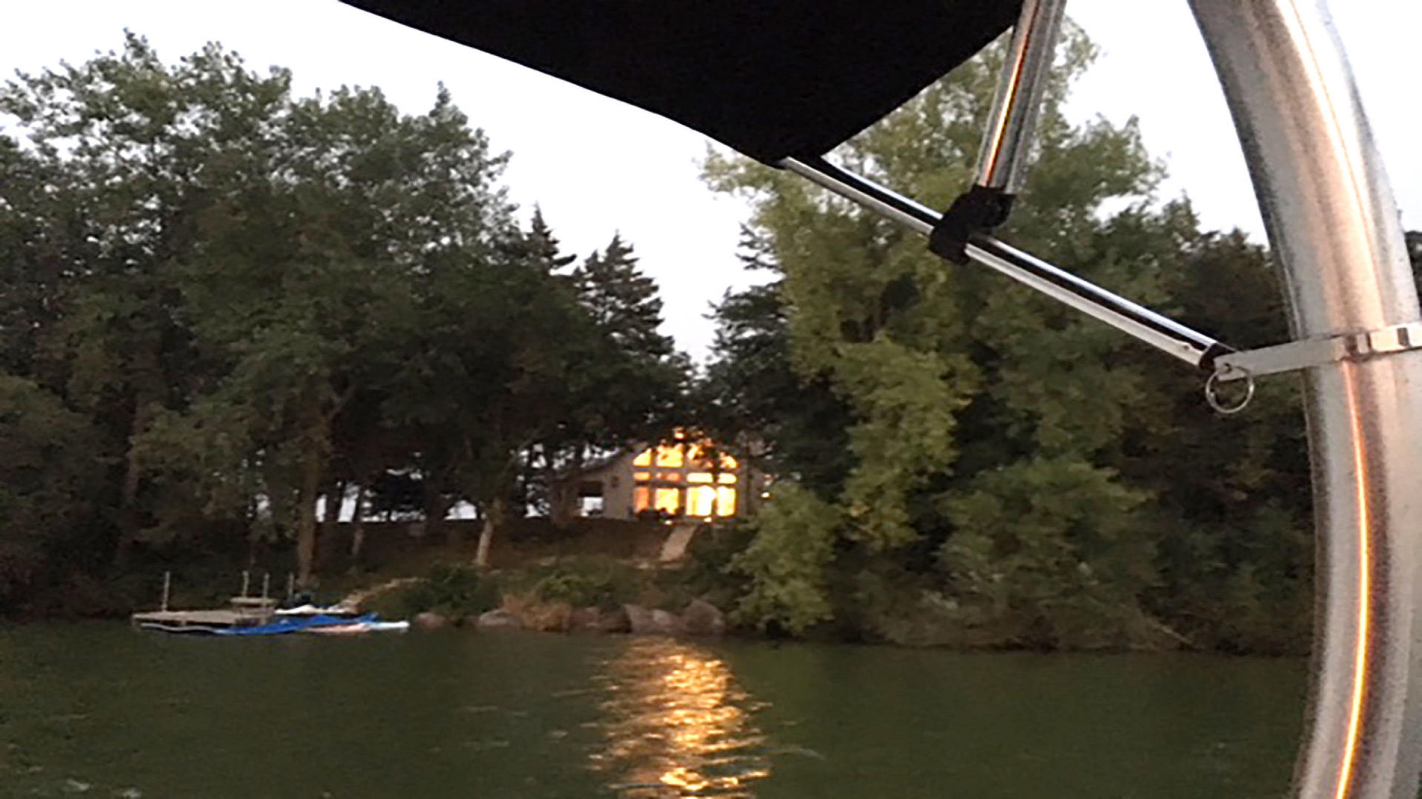 A tranquil lakeside view during twilight, featuring an illuminated house among the trees.