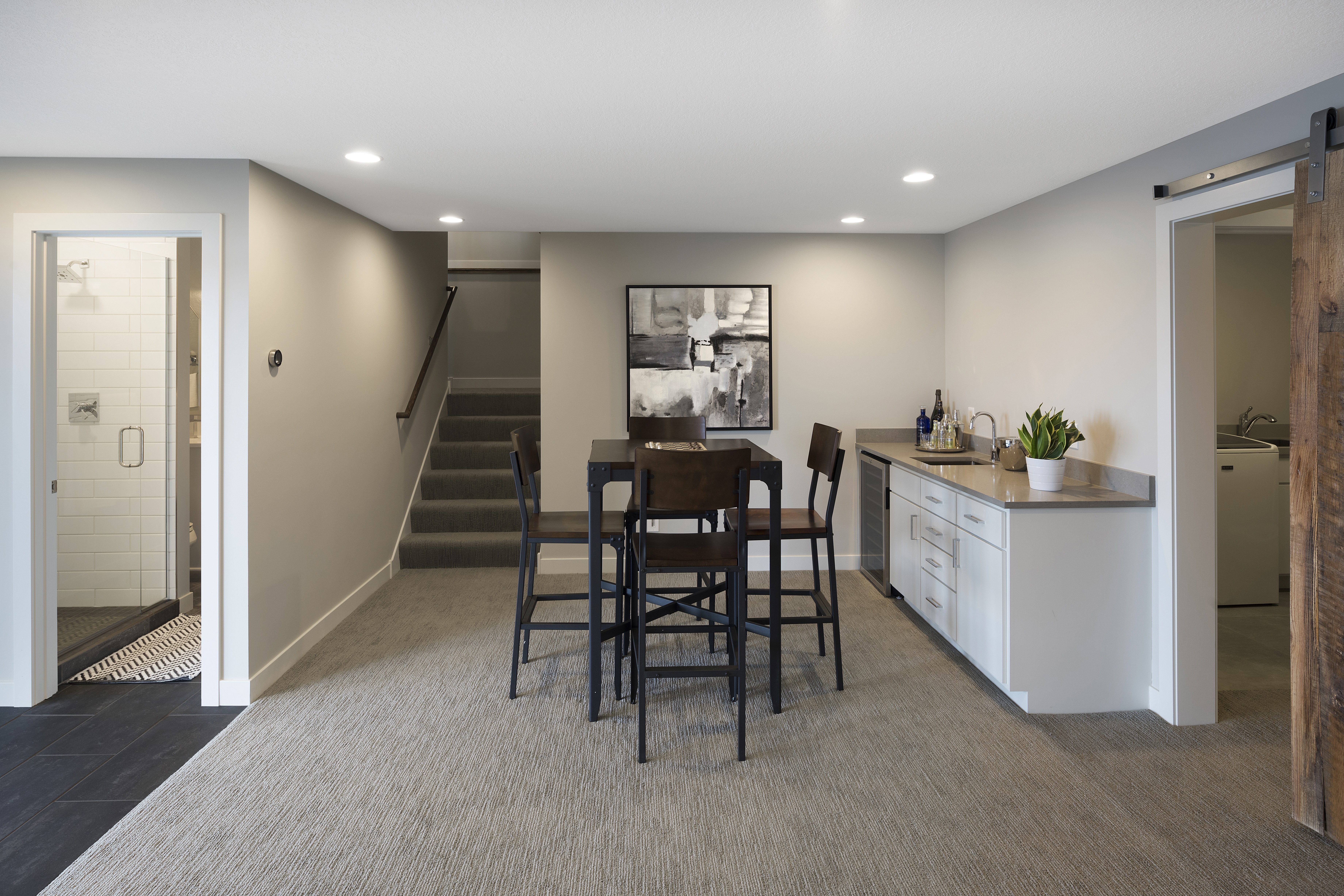 A modern basement living space featuring a dining area, kitchenette, and shower.