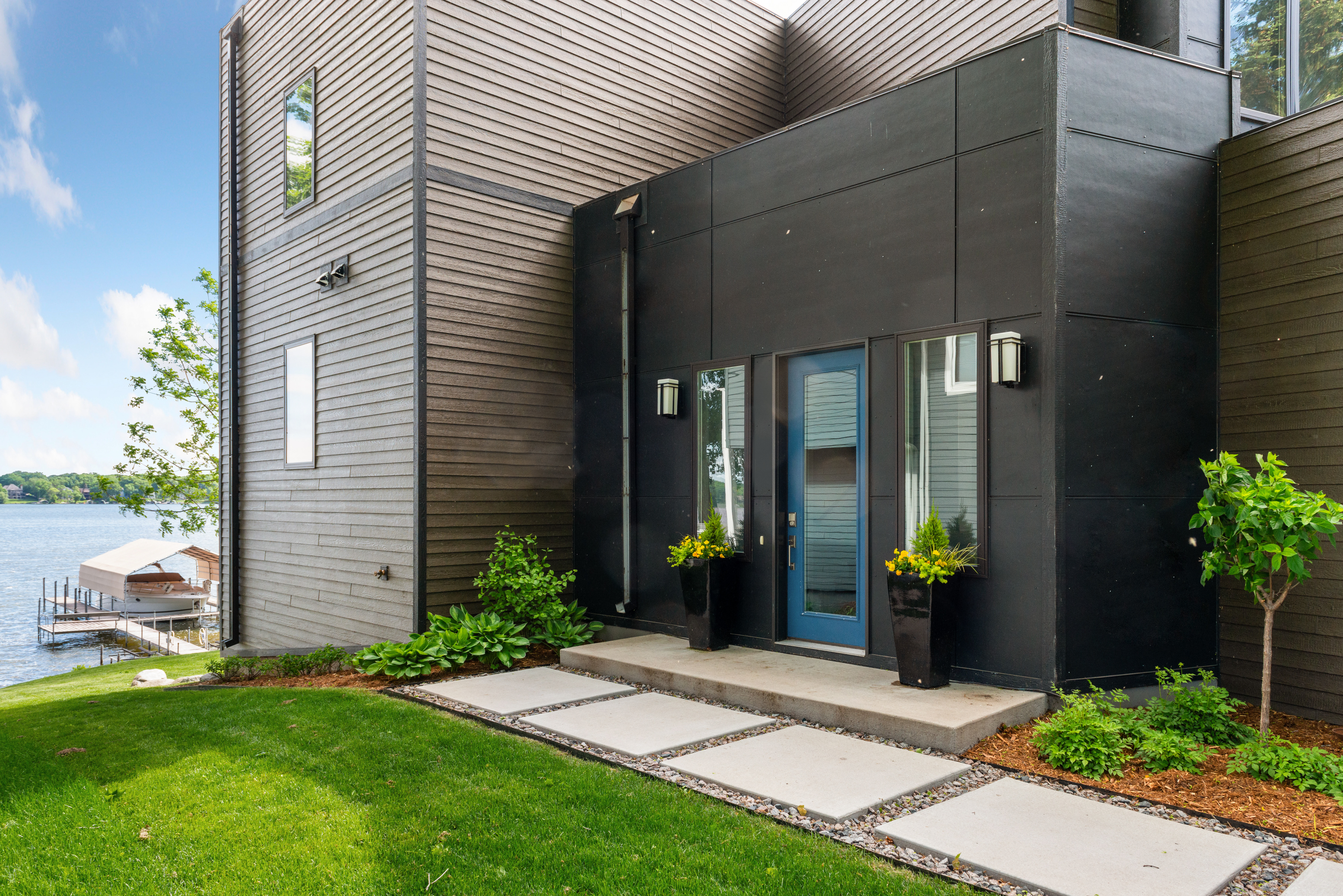 Modern lakeside home entrance with a vibrant blue door and lush greenery.