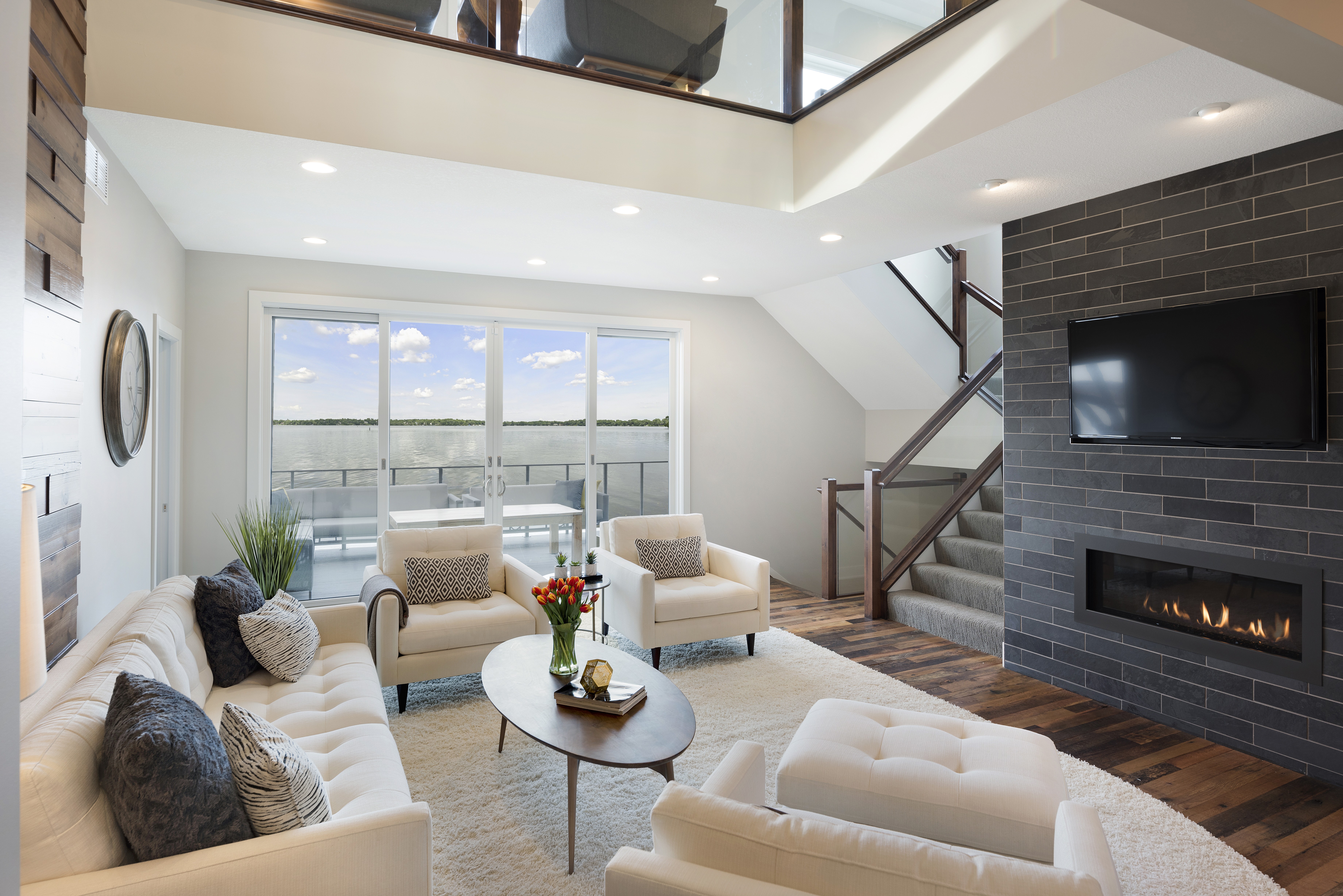 A modern living room with a waterfront view, featuring white furniture and a cozy fireplace.