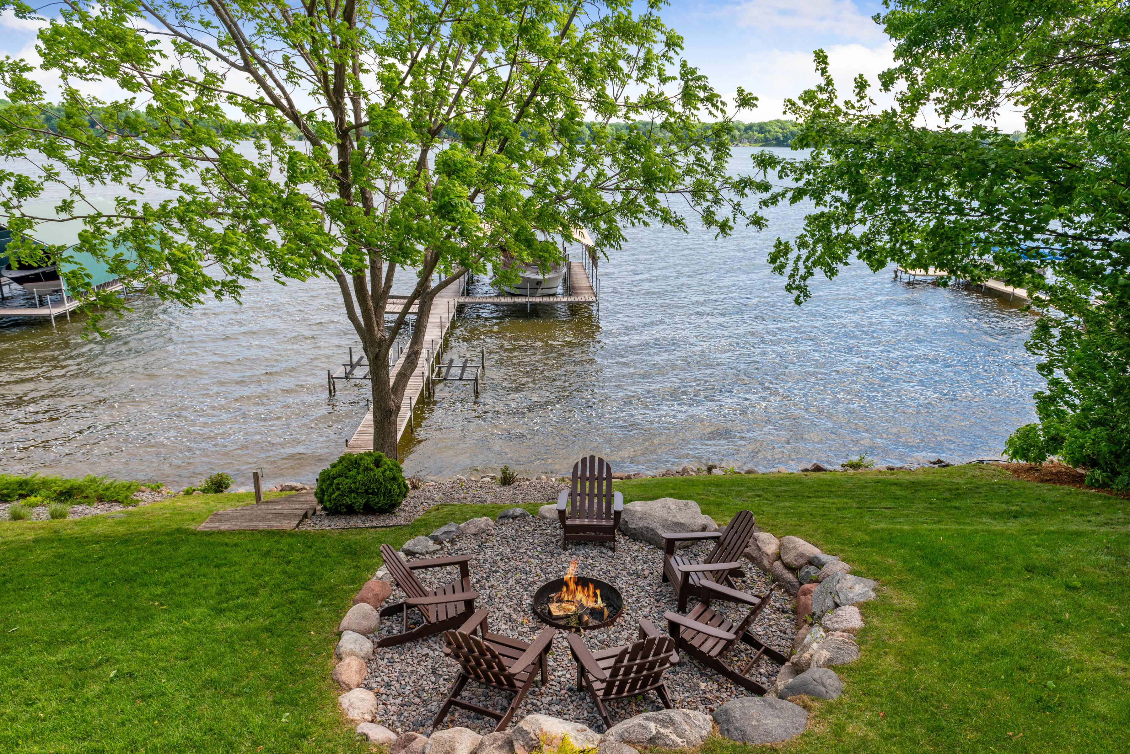 A cozy lakeside fire pit surrounded by Adirondack chairs, perfect for gatherings.
