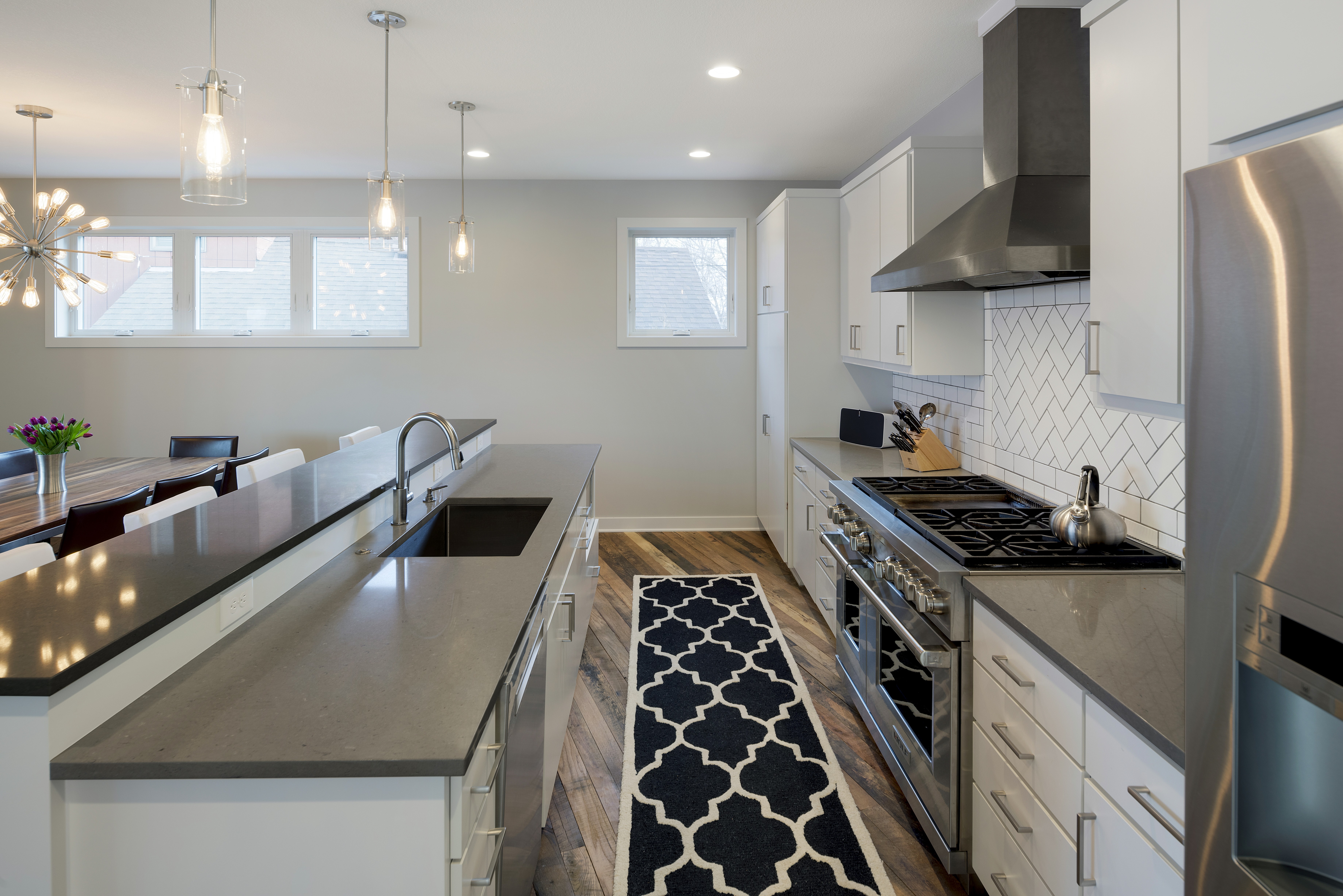 A contemporary kitchen with white cabinetry, a dark countertop, and stylish pendant lighting.