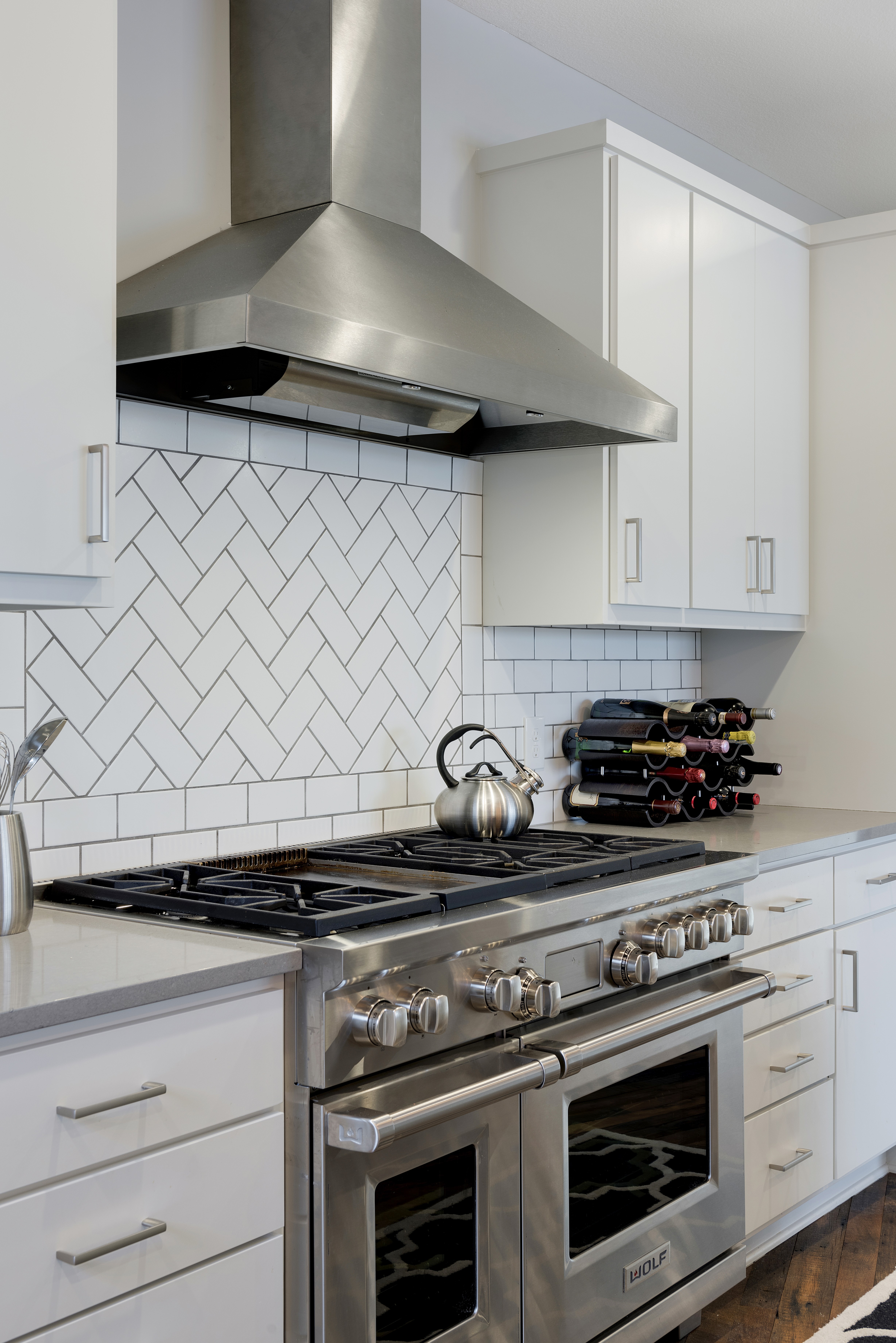 A modern kitchen with stainless steel appliances and a herringbone tile backsplash.