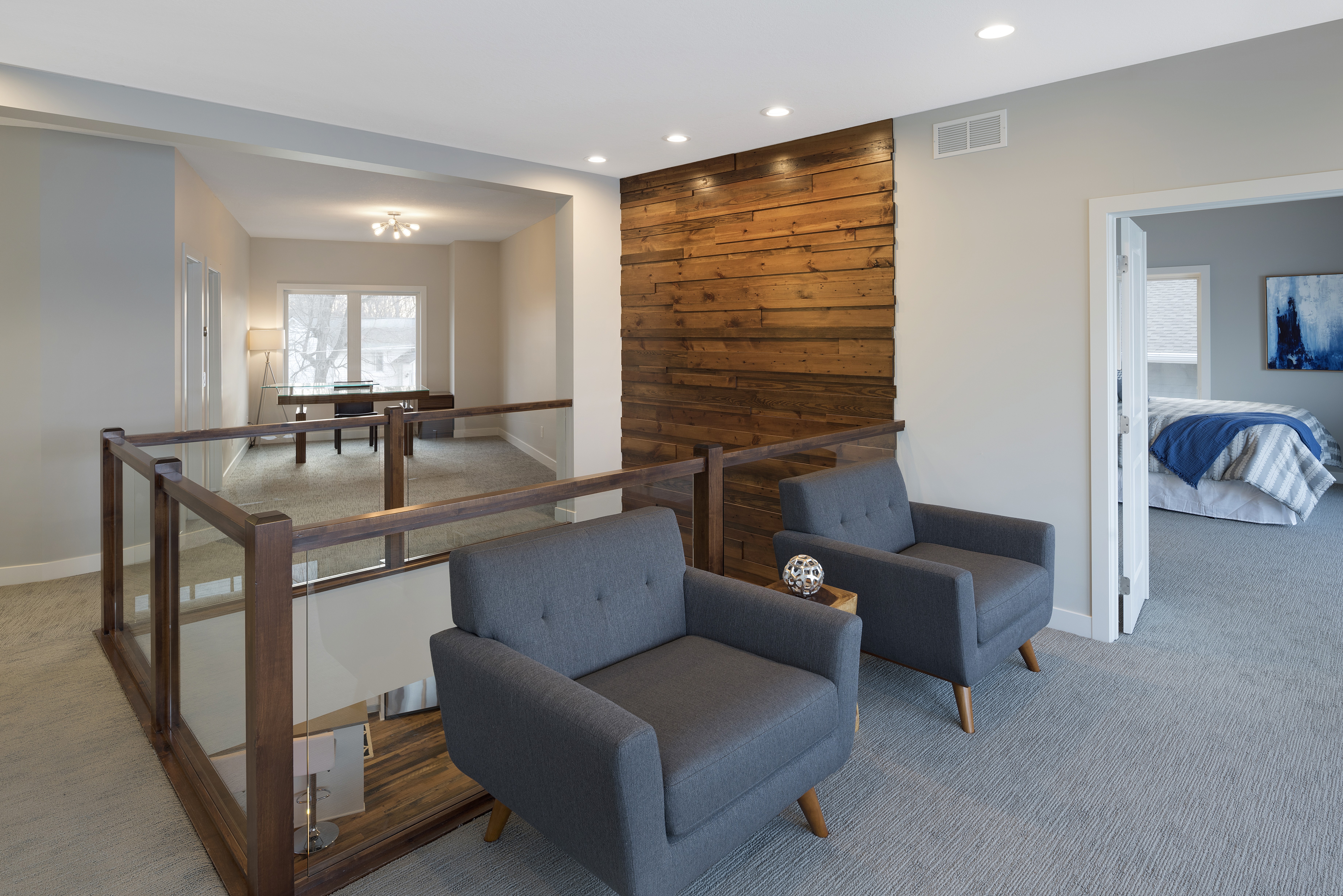 A modern loft interior featuring gray armchairs and a wooden accent wall.