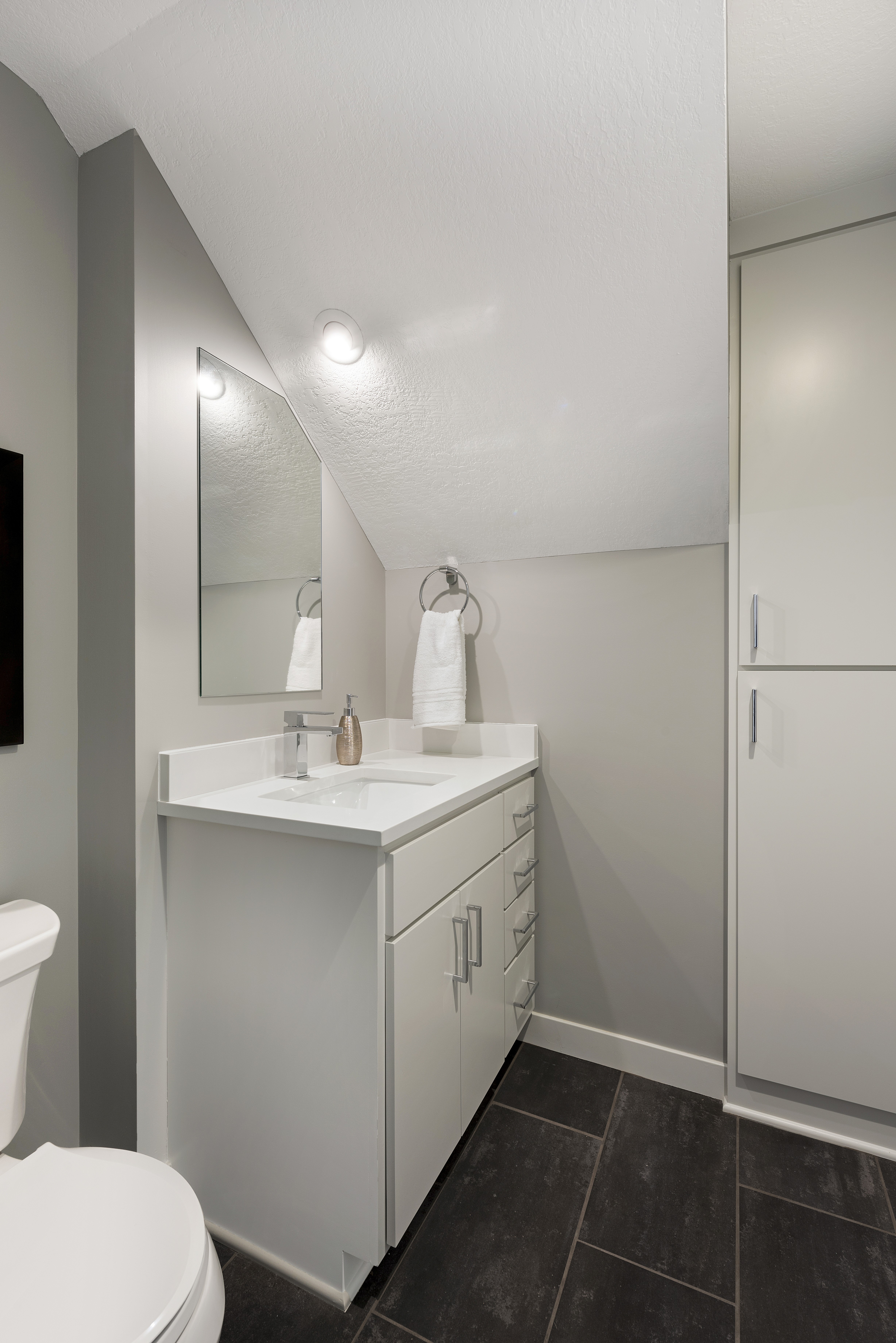 A modern and minimalist bathroom featuring a sleek white vanity and dark flooring.