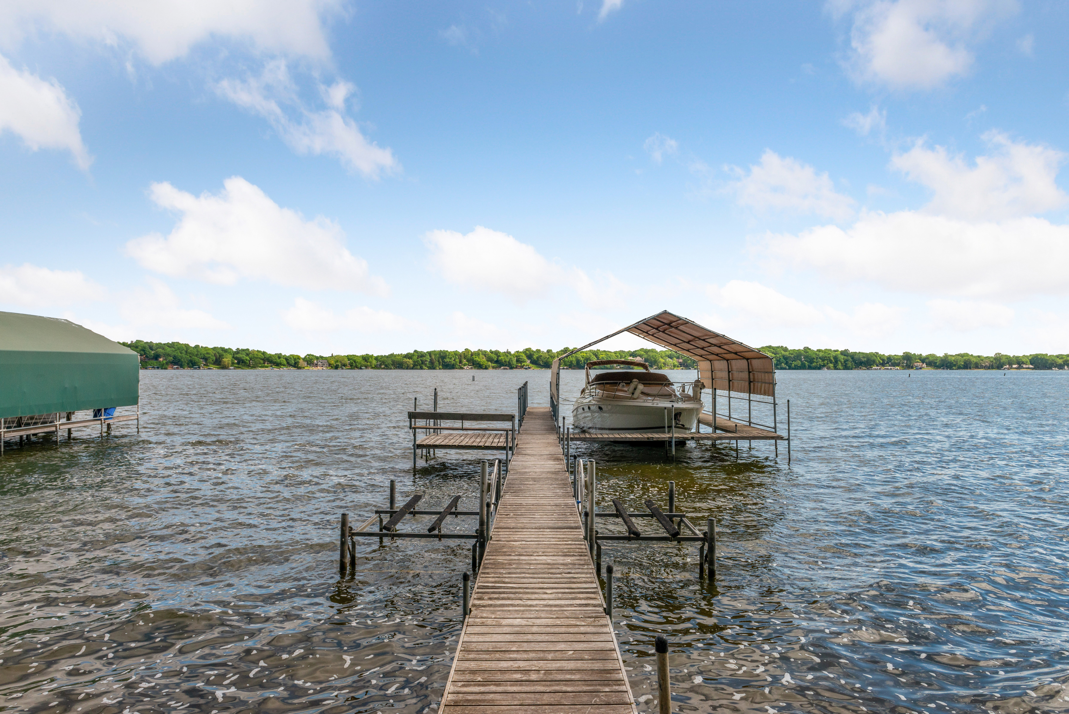 A peaceful lakeside dock with a boat under cover and trees in the background.