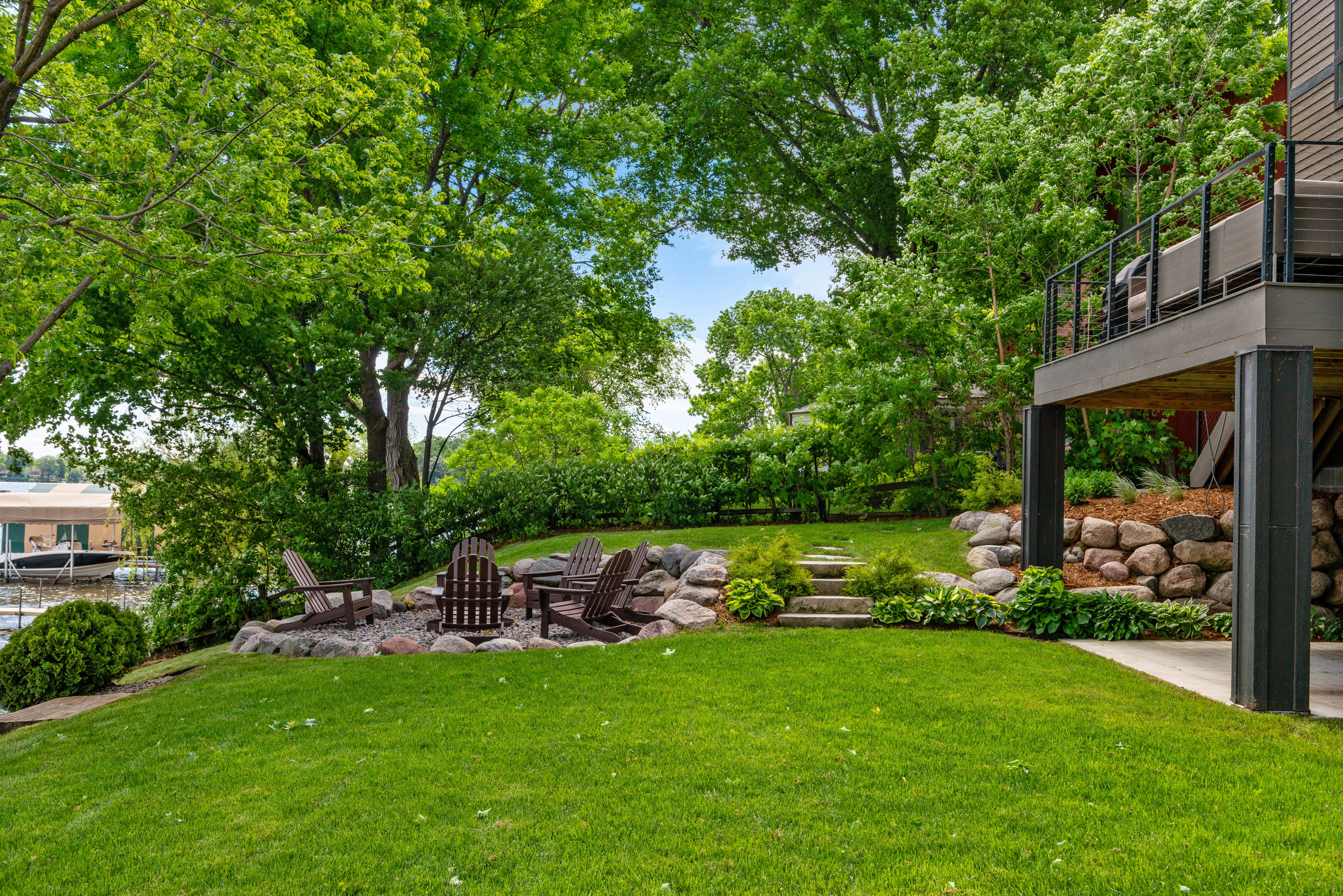 A tranquil outdoor space with a fire pit and Adirondack chairs surrounded by greenery.