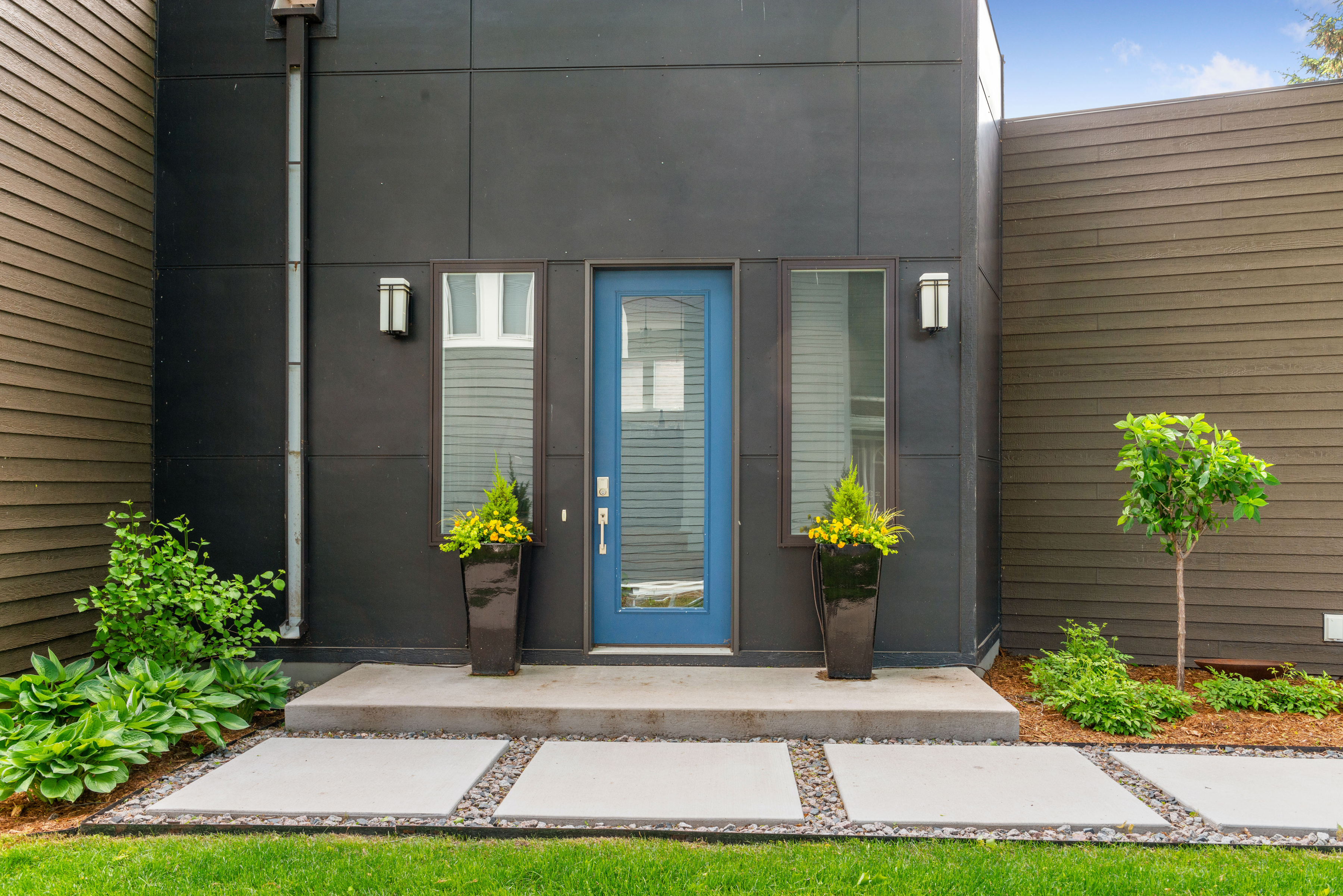 A modern home entryway featuring a blue front door and stylish planters.