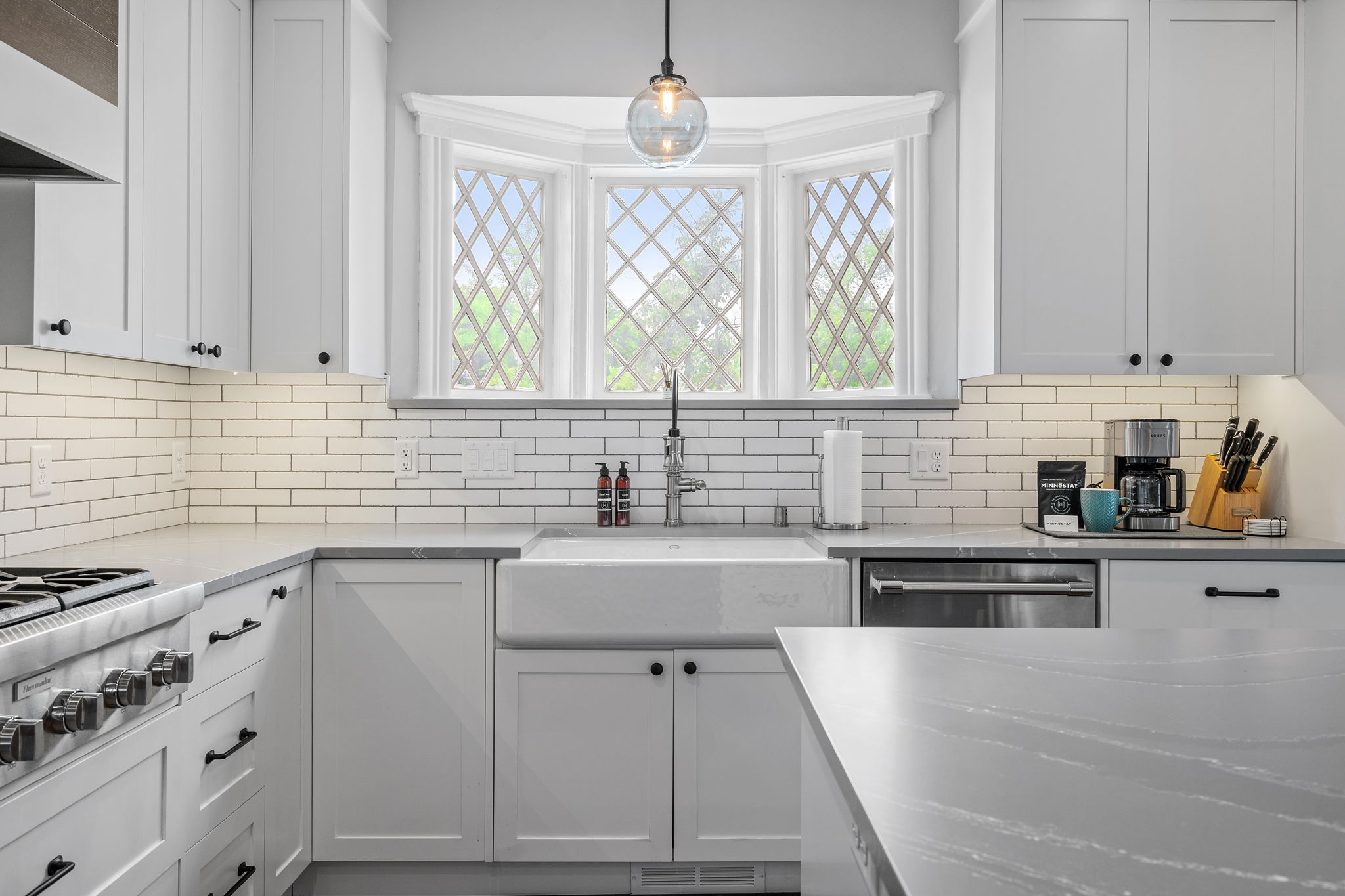 A modern kitchen with bright white cabinetry and a farmhouse sink beneath a bay window.