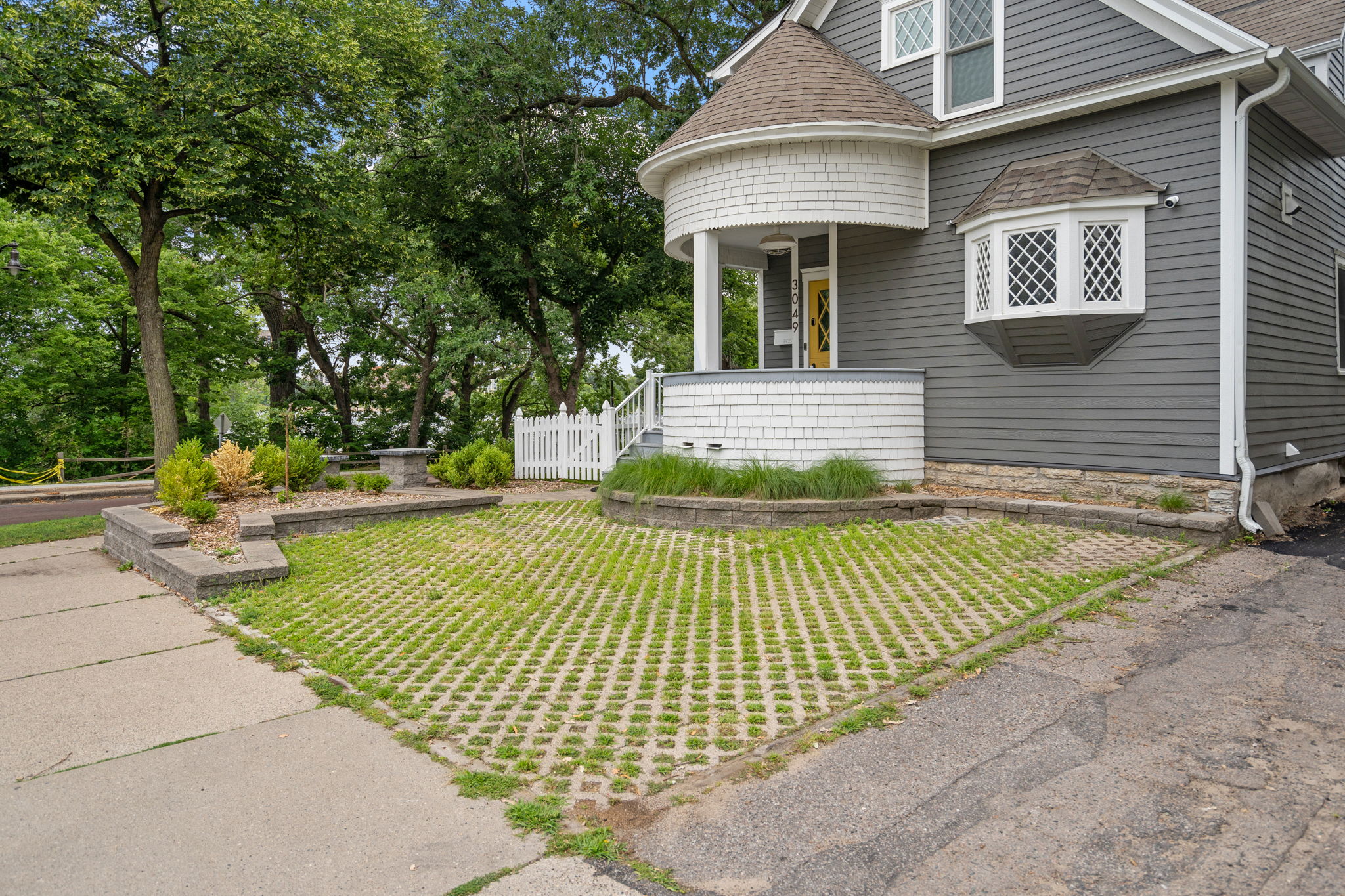 Charming exterior of a multi-story gray house with a unique porch and landscaped yard.