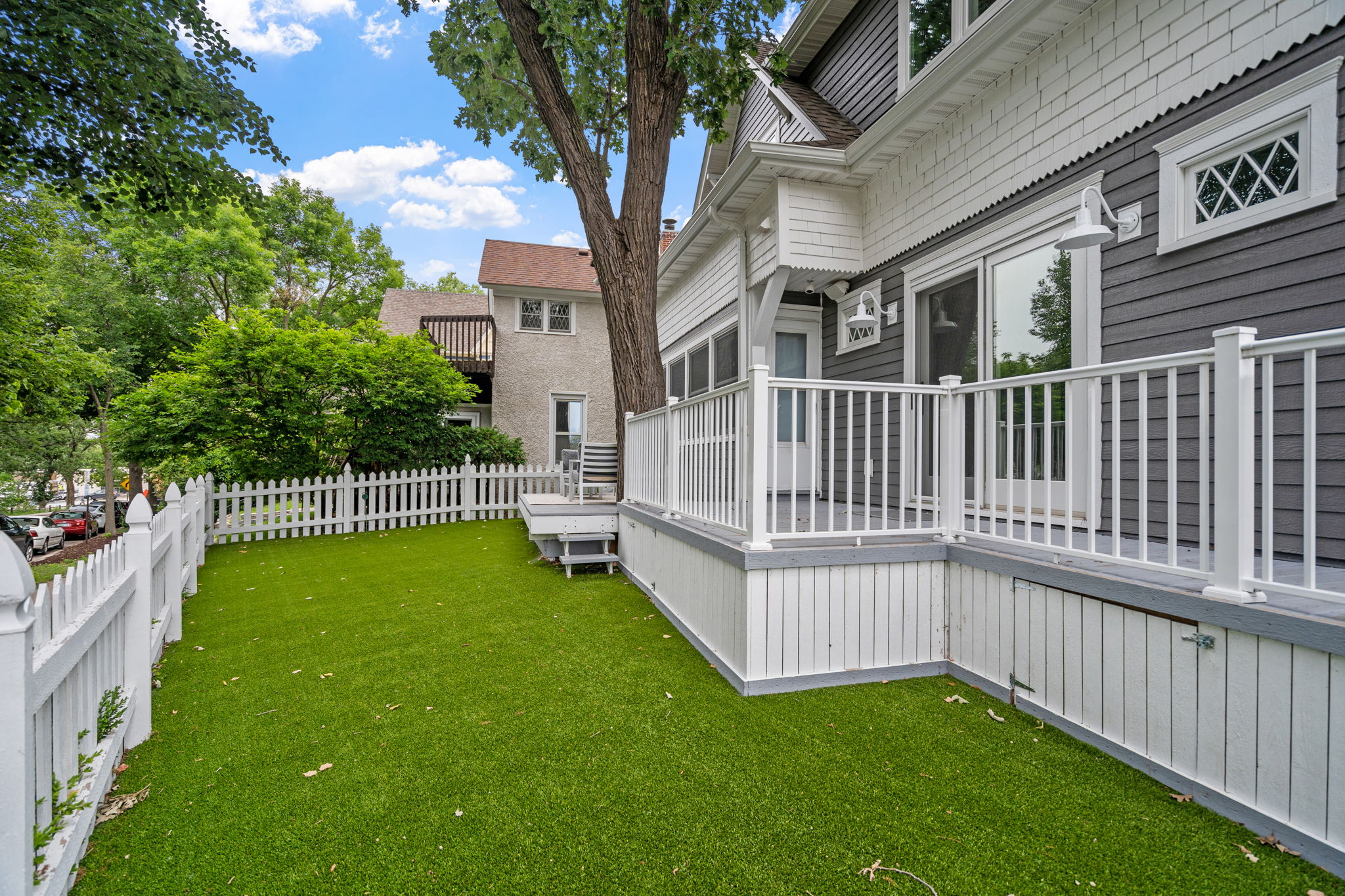 A charming suburban yard enclosed by a white picket fence with a stylish house in the background.