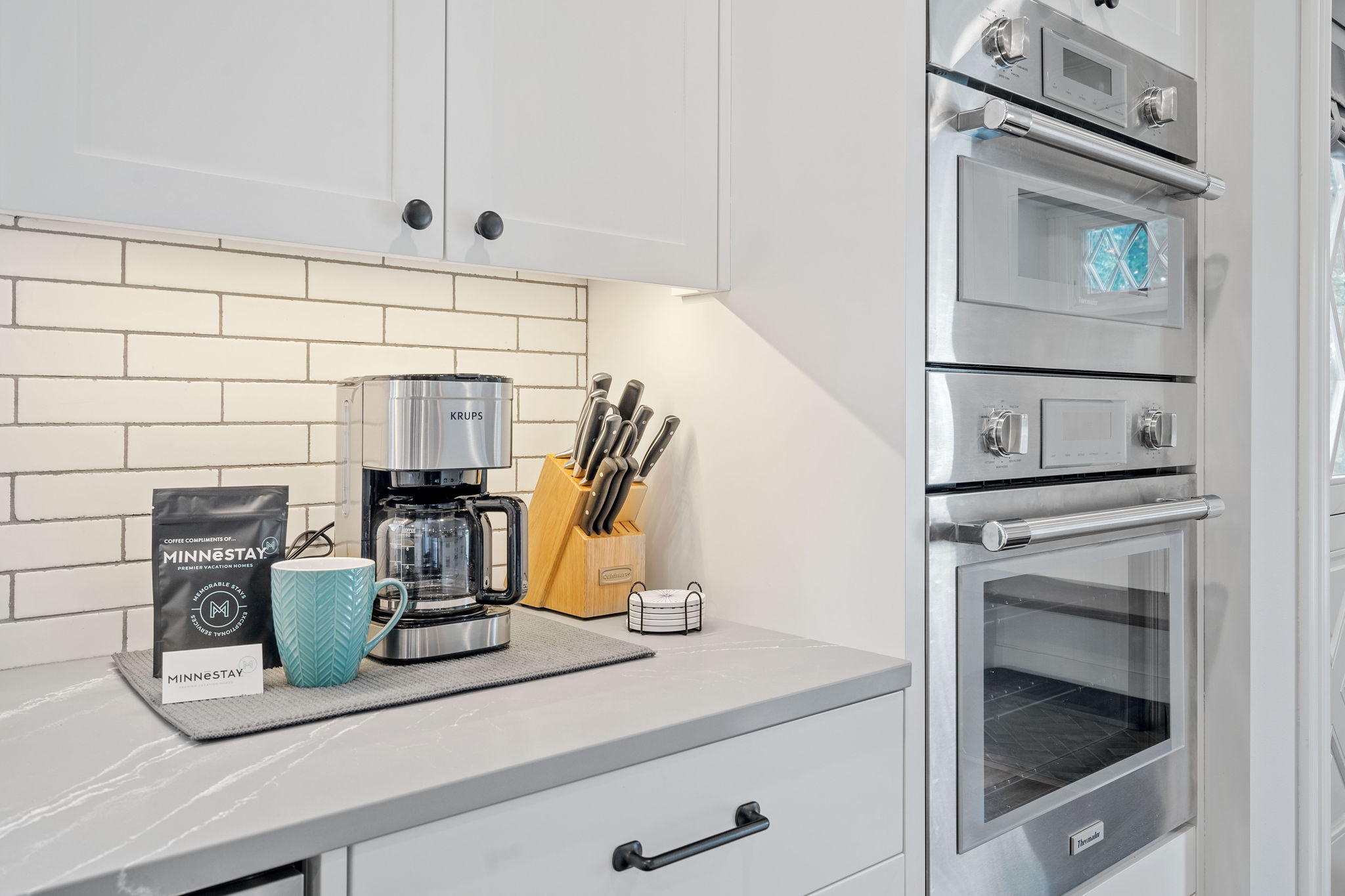 A modern kitchen featuring a KRUPS coffee maker, textured mug, and stainless steel appliances.
