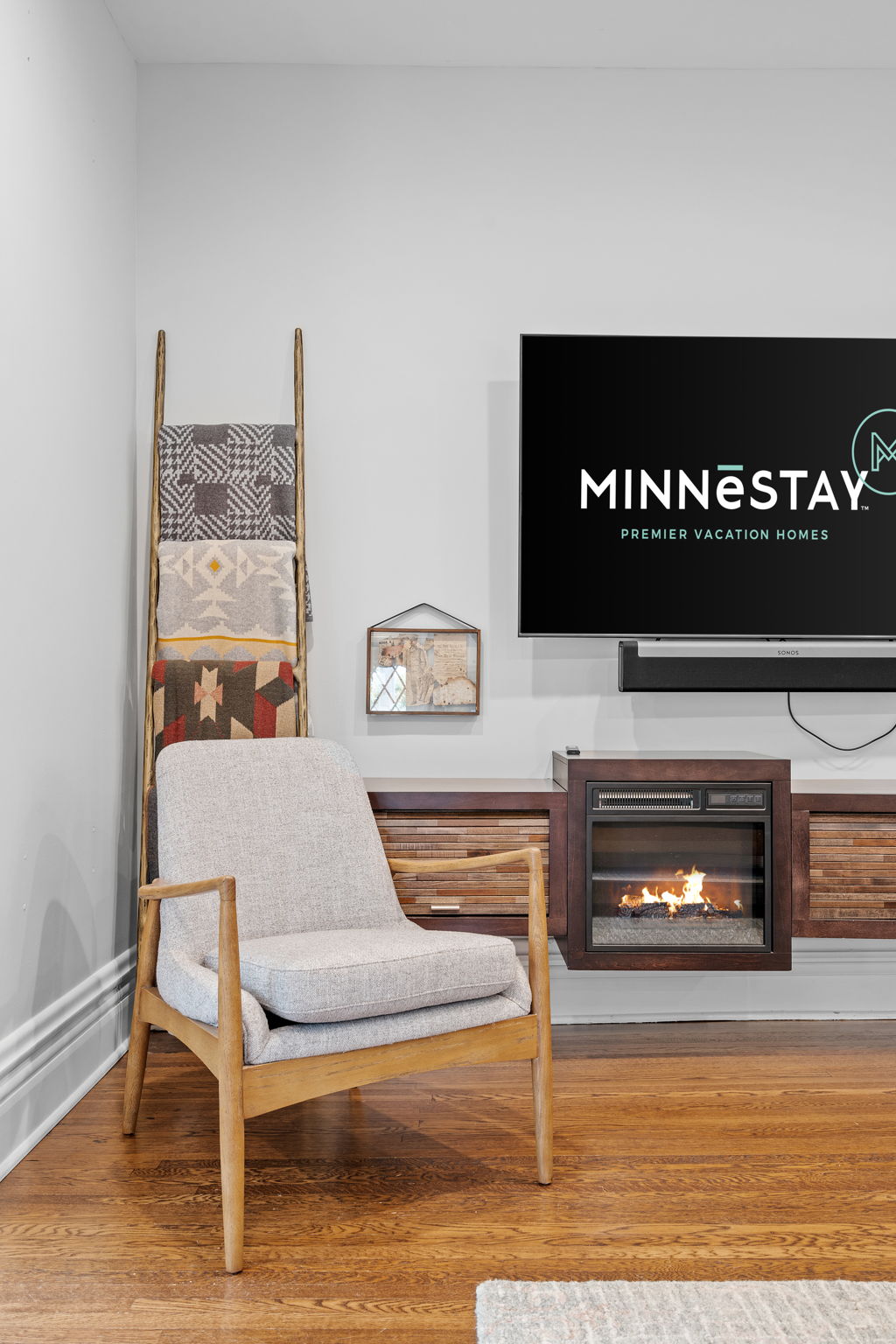 A cozy living room featuring a modern armchair, blankets, and an electric fireplace.