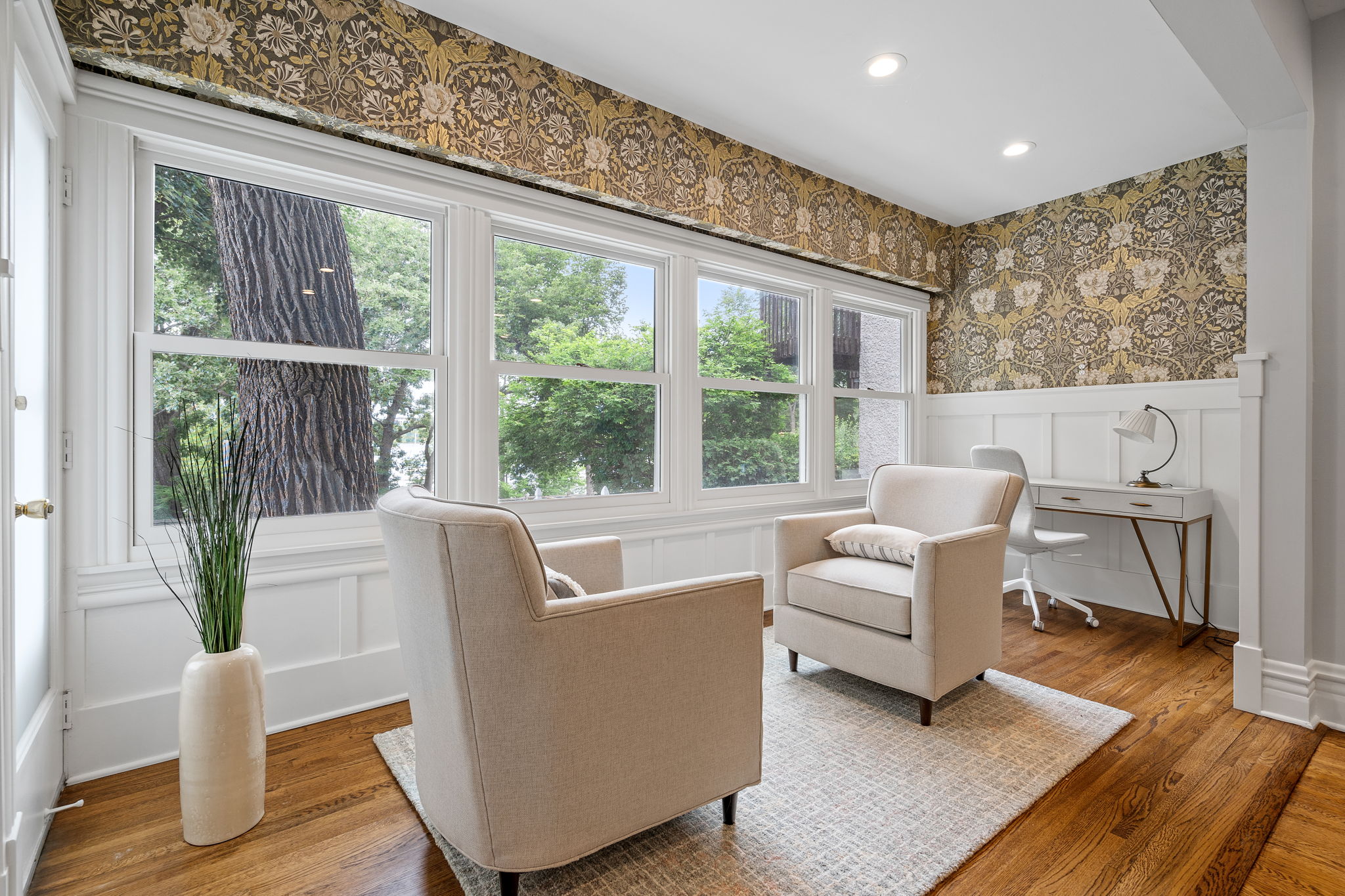 A cozy modern sitting area with natural light, elegant wallpaper, and a small desk.