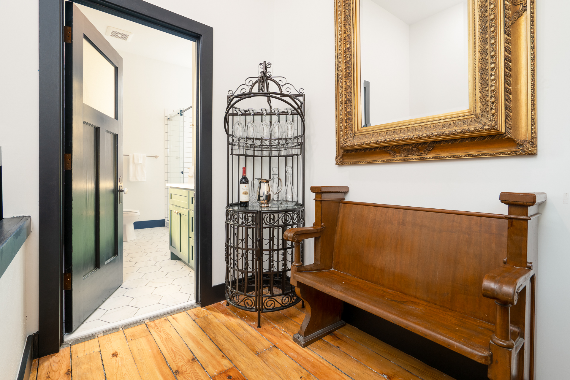 A stylish entryway featuring a wooden bench, wine rack, and a glimpse of a bathroom.