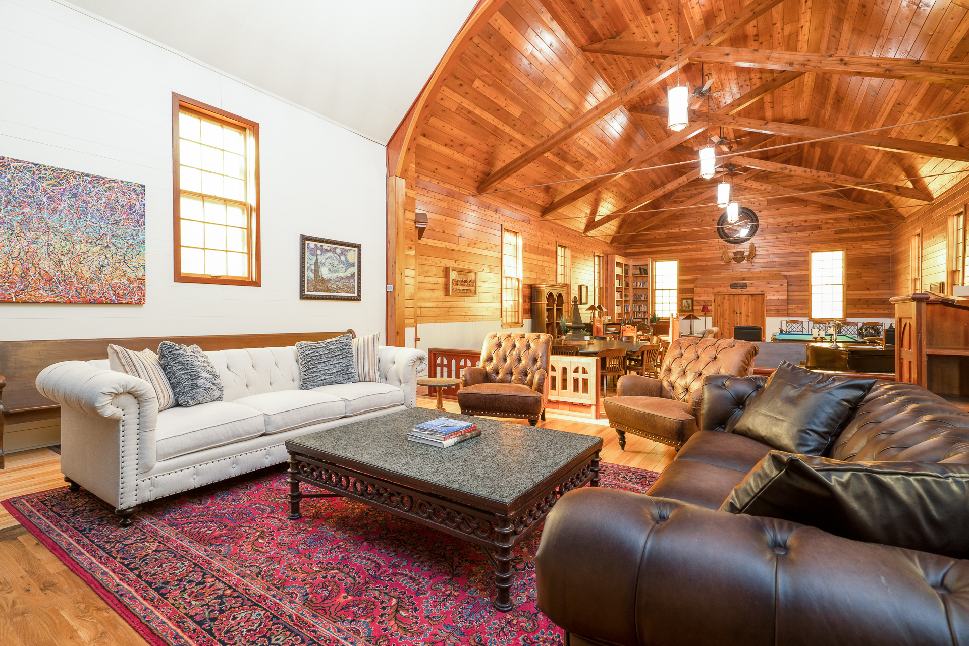 Spacious living room with high wooden beams, plush furniture, and artworks on the walls.