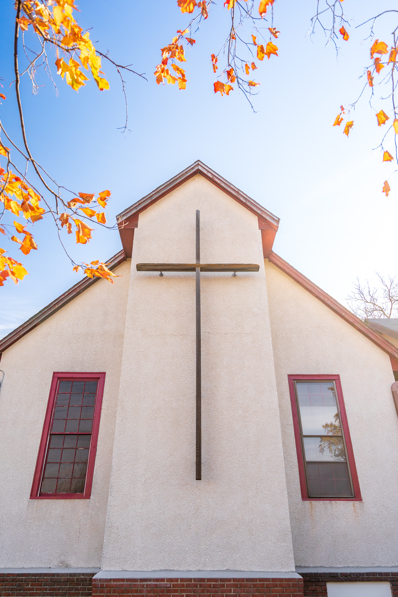 A church front adorned with a cross, framed by autumn leaves.