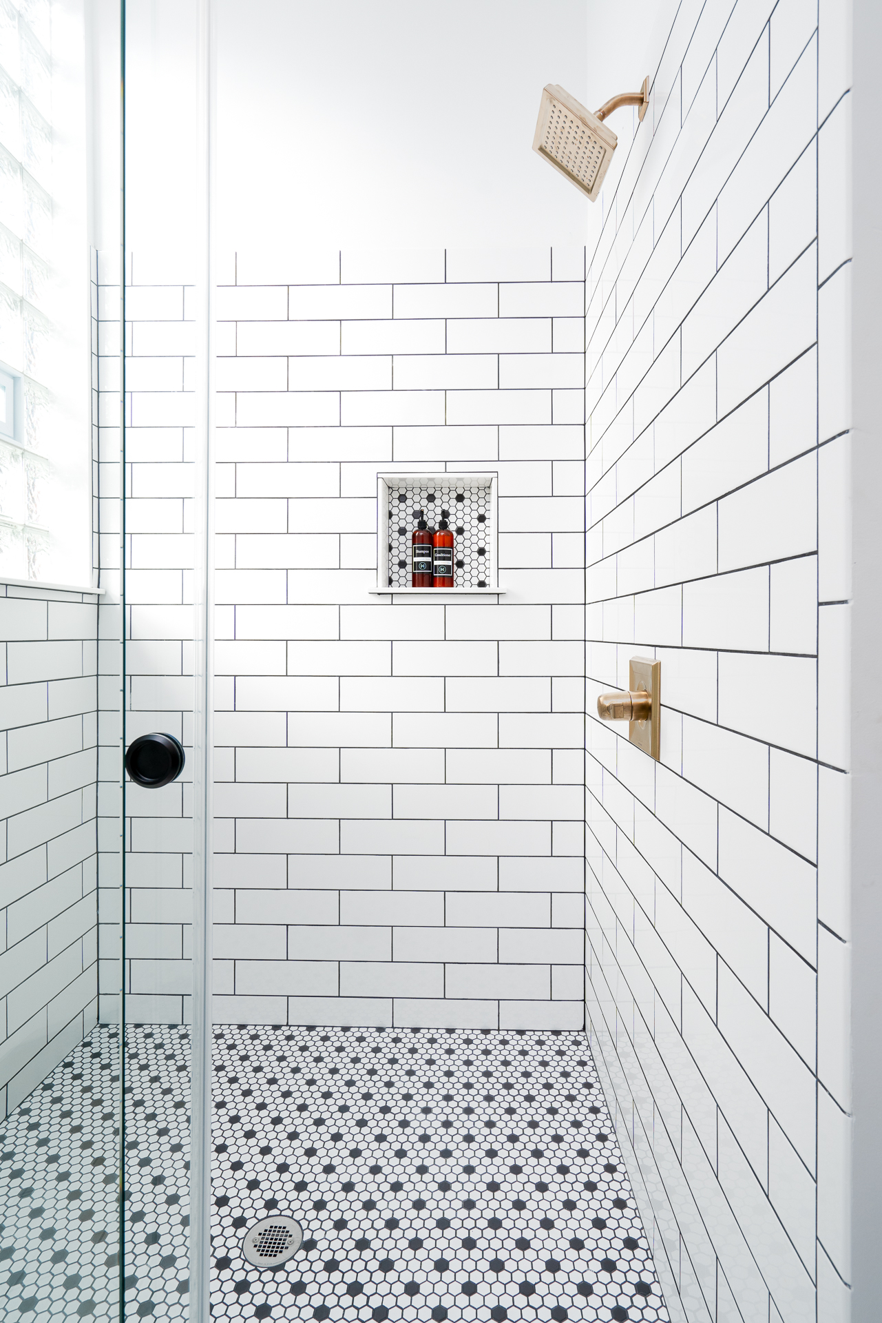 A sleek, modern shower featuring white subway tiles and hexagonal flooring.