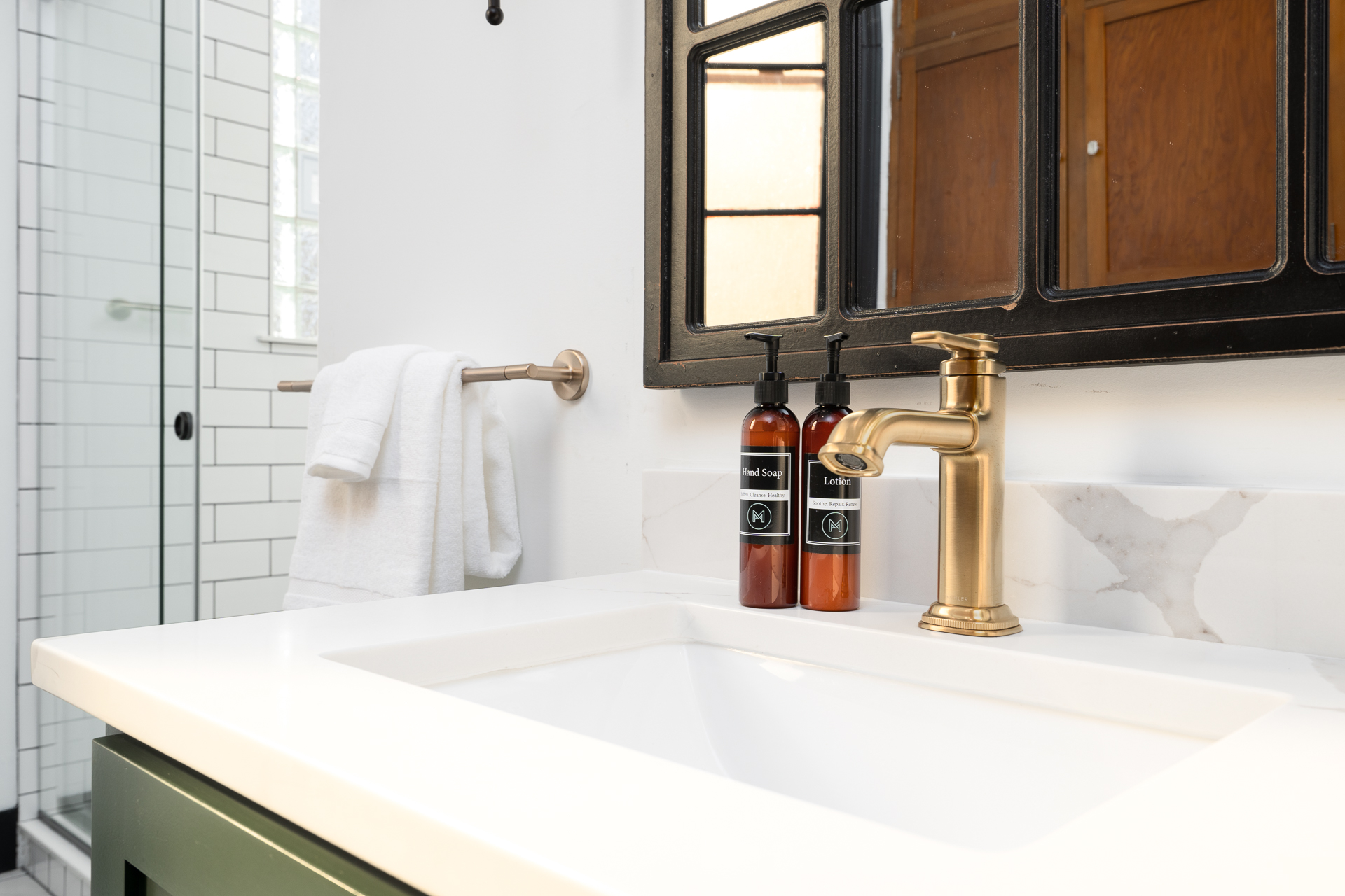 A modern bathroom featuring a stylish gold faucet, amber lotion bottles, and a white sink.