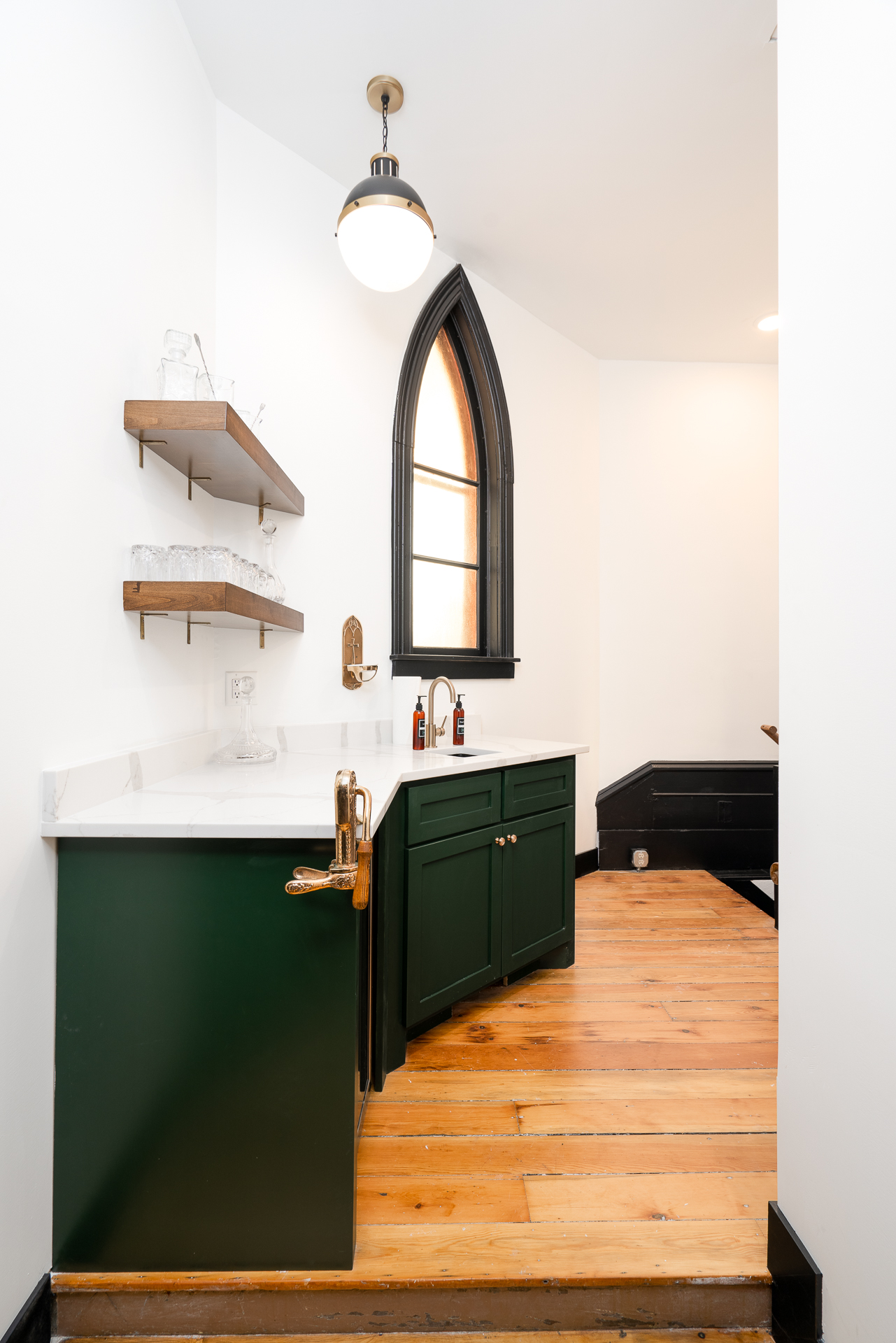 A stylish small kitchen area with green cabinetry and elegant wooden shelves.