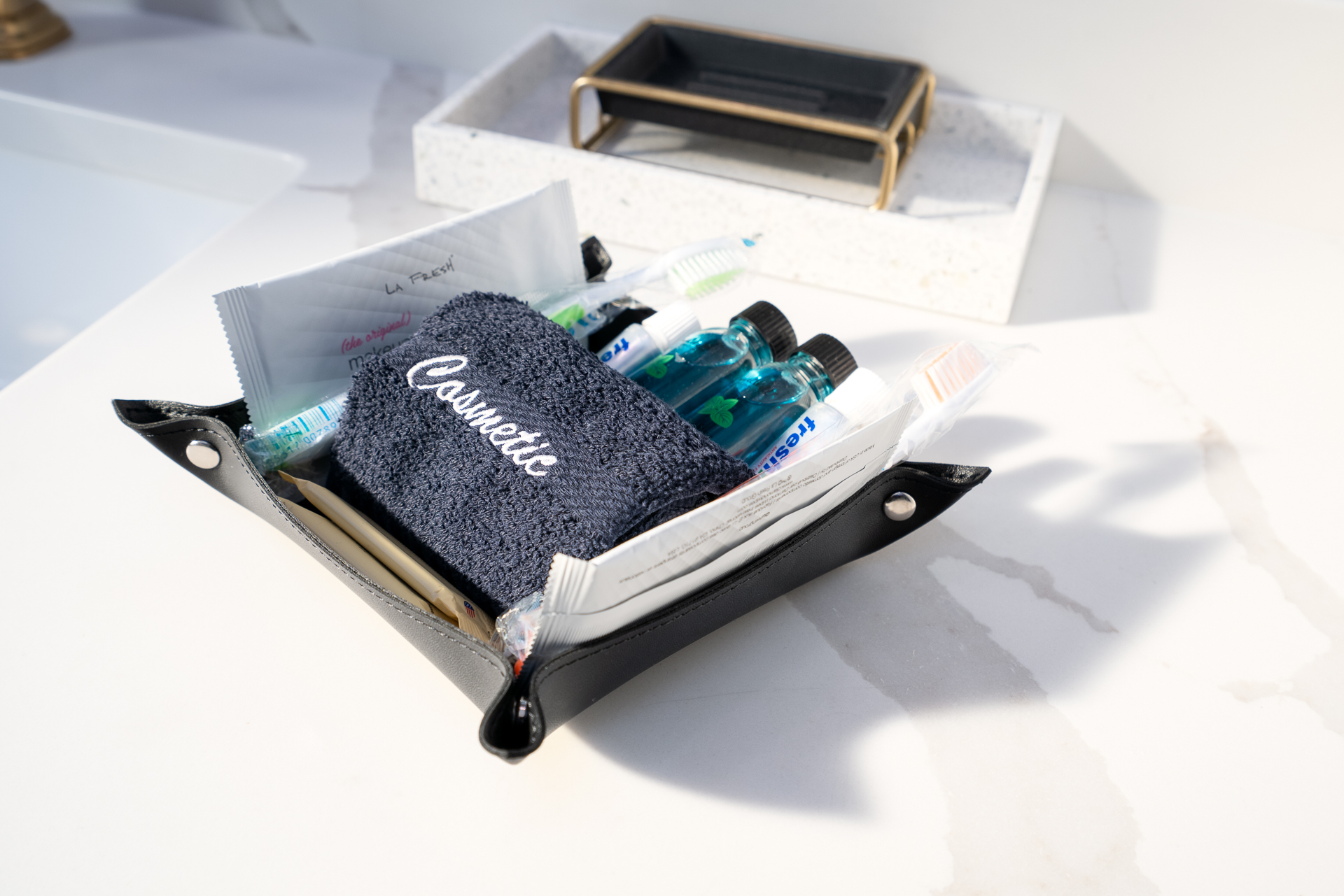 A neatly organized black cosmetic pouch filled with personal care essentials on a marble surface.