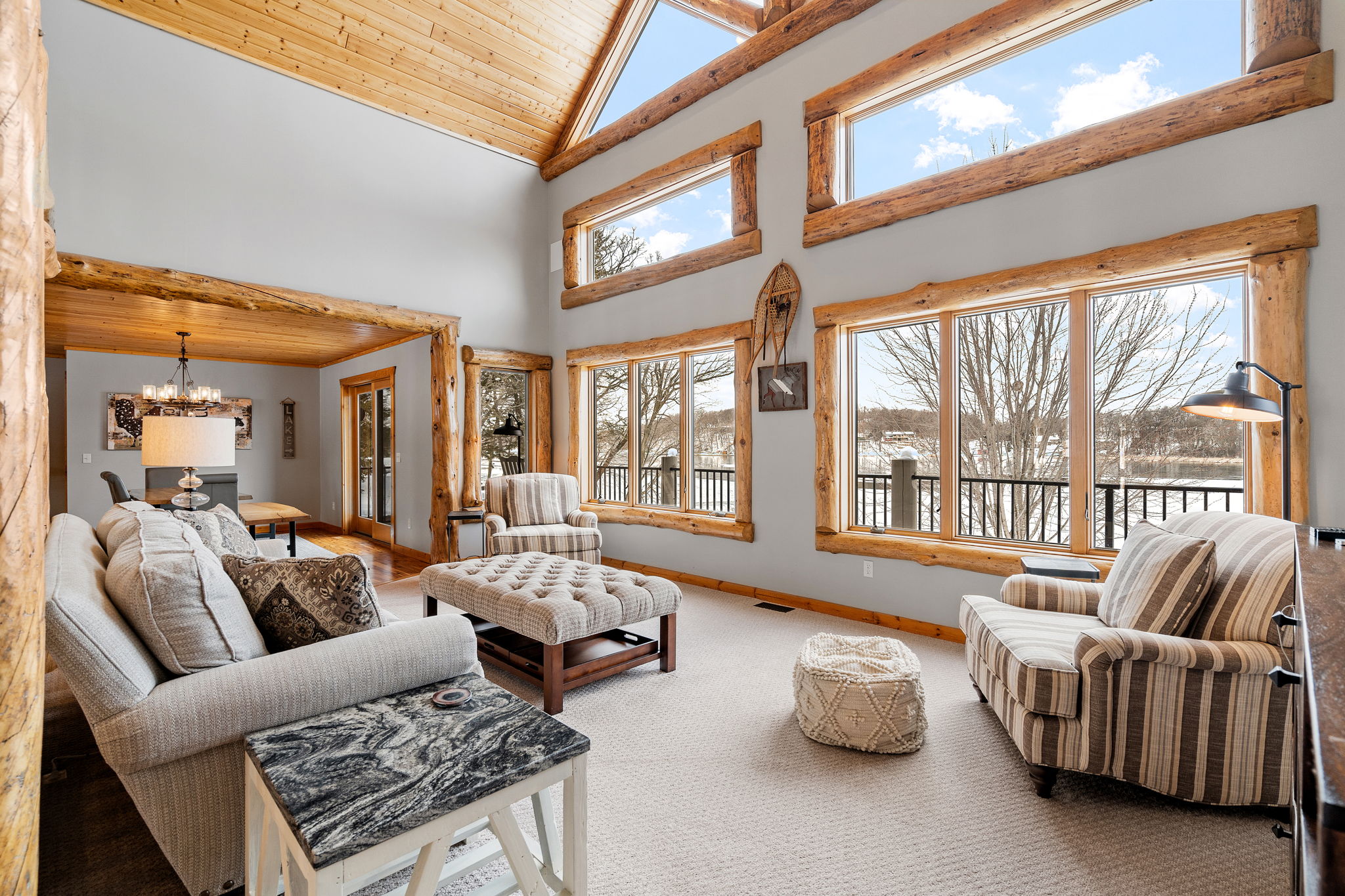 A bright living room with high ceilings, wooden beams, and large windows overlooking a natural landscape.