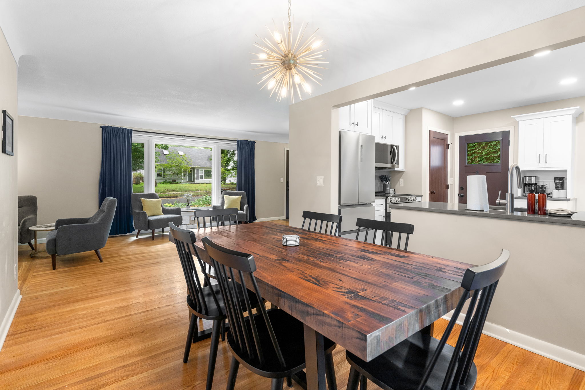 Interior of a modern dining area with a large wooden table, contemporary chandelier, and a cozy reading nook by the window.