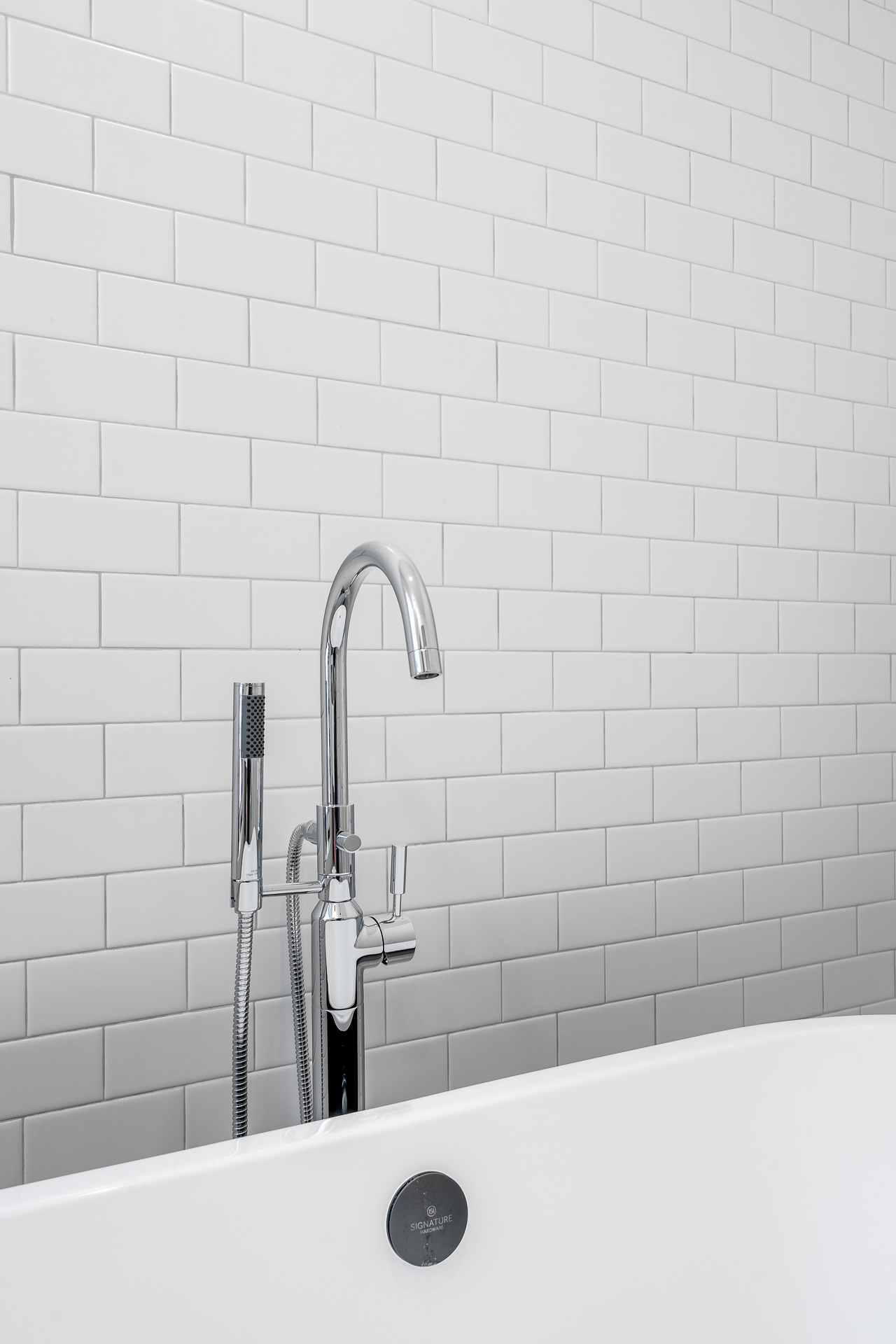 A modern bathroom featuring a sleek white bathtub and chrome faucet against white subway tiles.