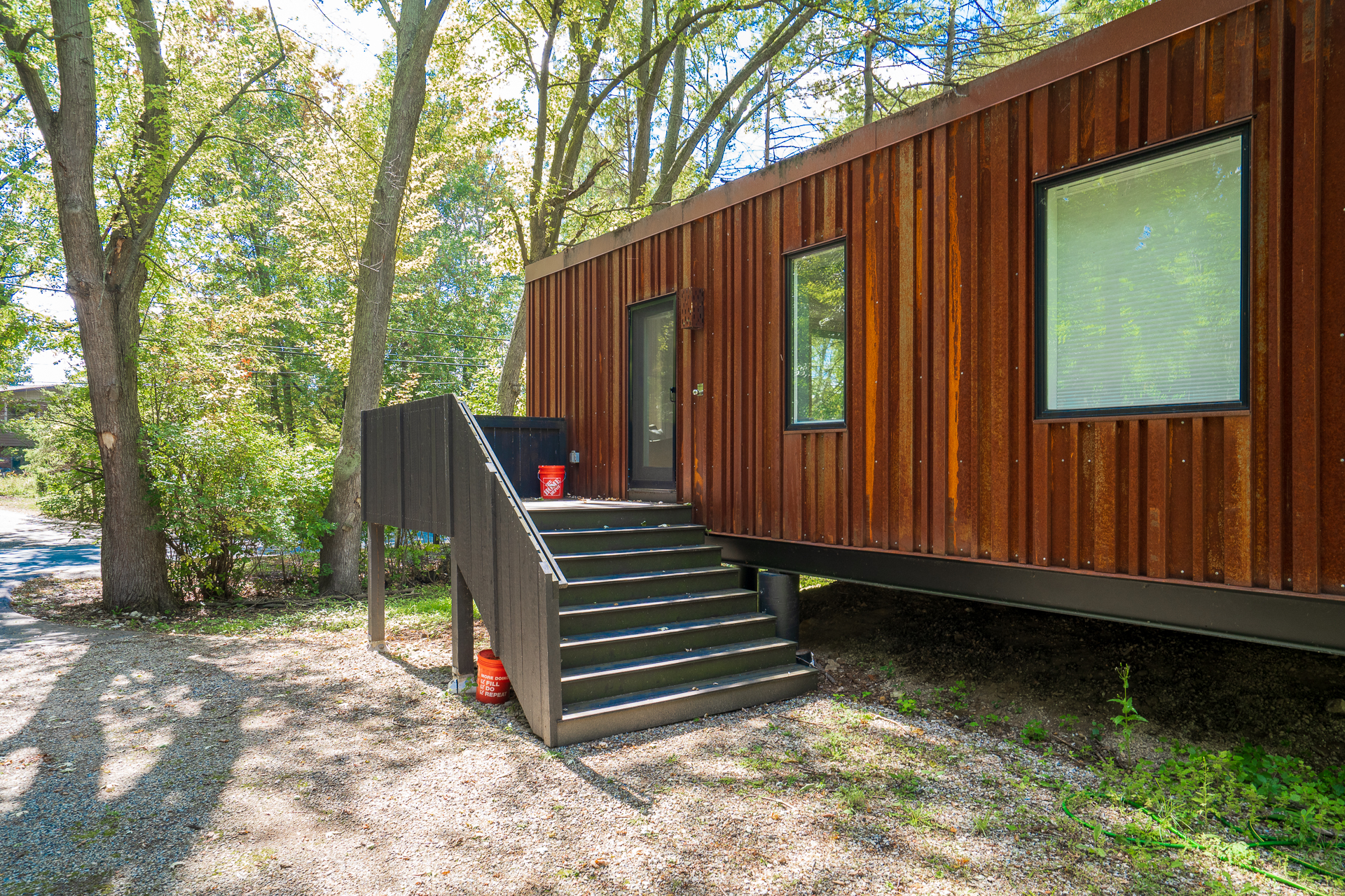 A modern elevated home with rust-colored siding surrounded by lush greenery.