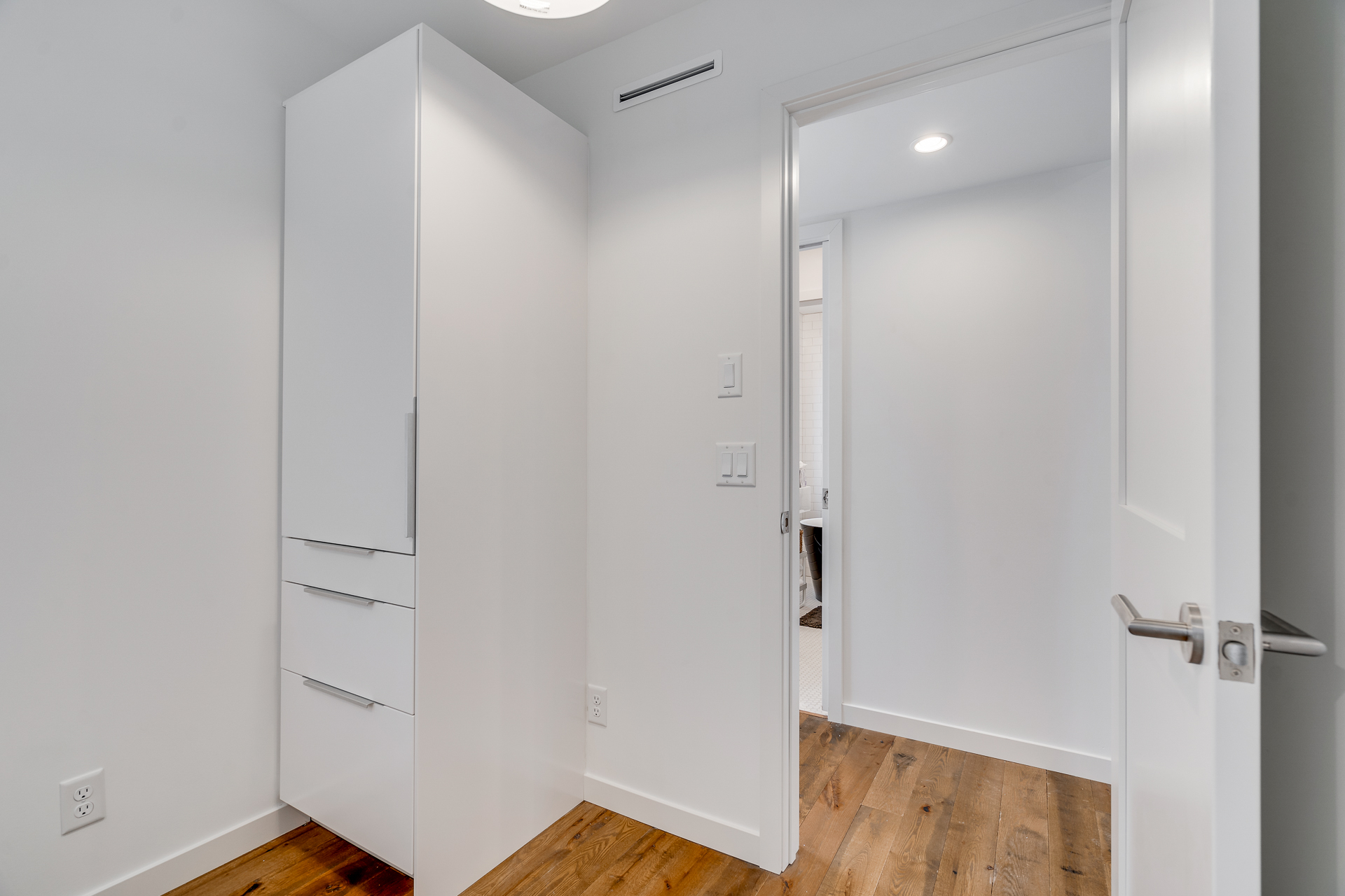 A sleek modern hallway featuring a tall white cabinet and an inviting open doorway.