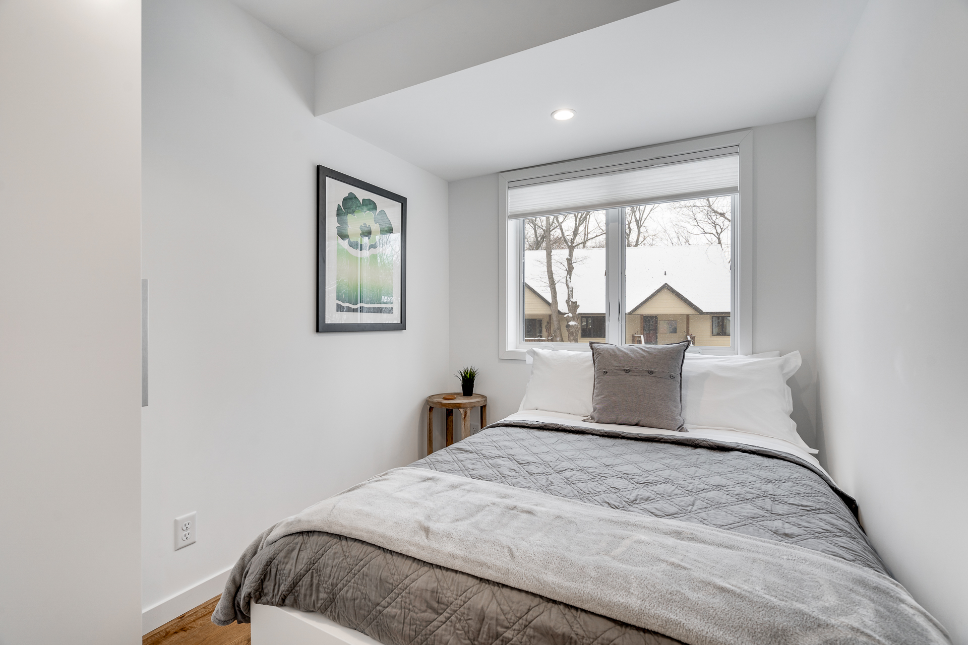 A cozy and minimalist bedroom with a view of snow-covered rooftops.