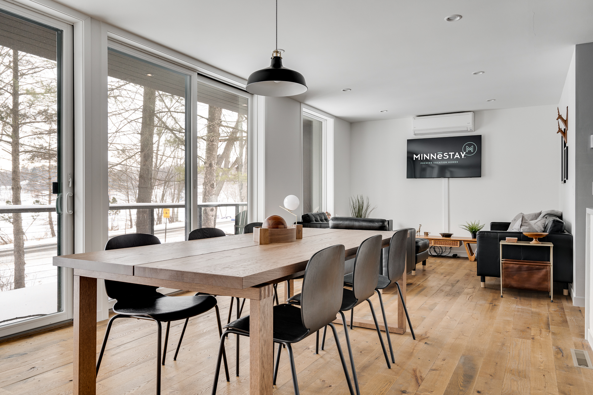 Modern dining area with a rustic table and sleek black chairs, overlooking a winter landscape.