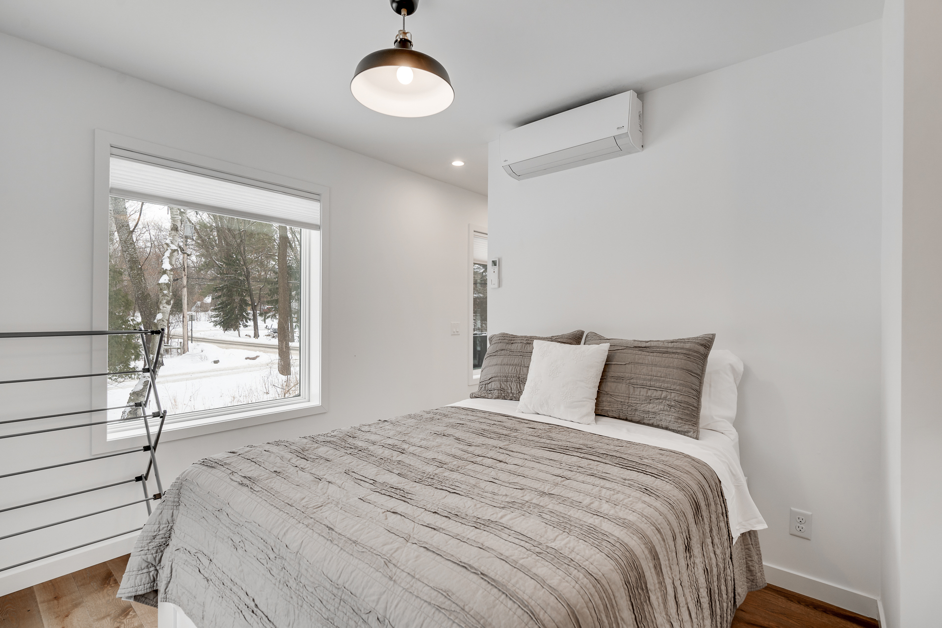 A peaceful, minimalist bedroom adorned with a textured gray quilt and large windows overlooking a snowy landscape.
