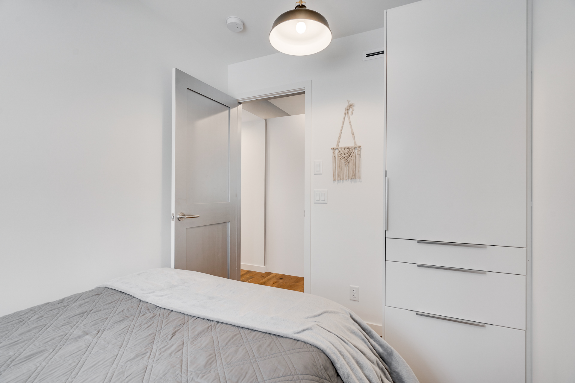A modern and minimalist bedroom featuring a gray bedspread and sleek furnishings.