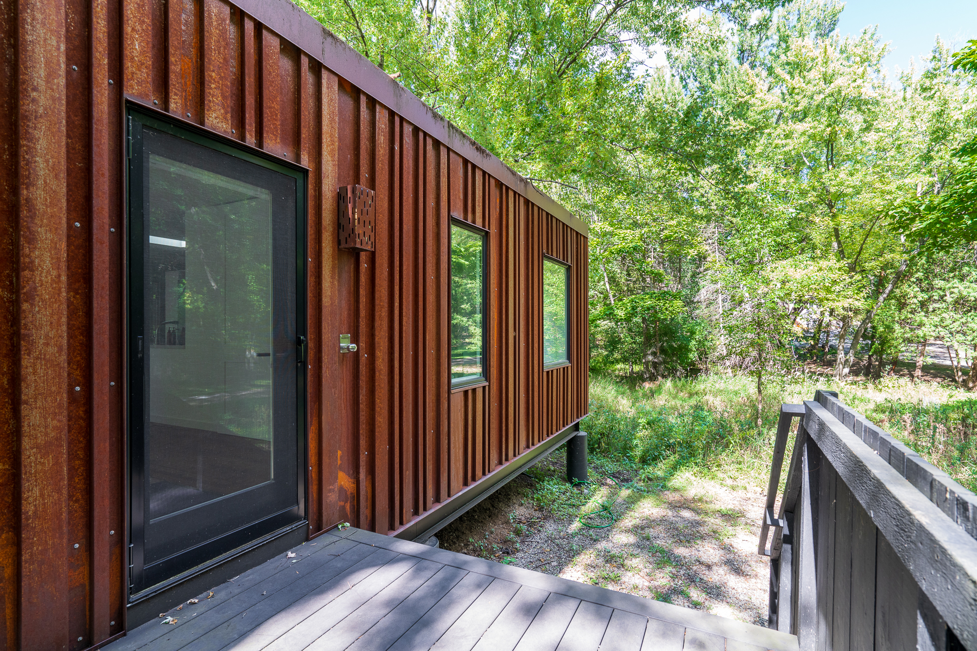 A modern rustic building with a weathered exterior, surrounded by lush greenery.